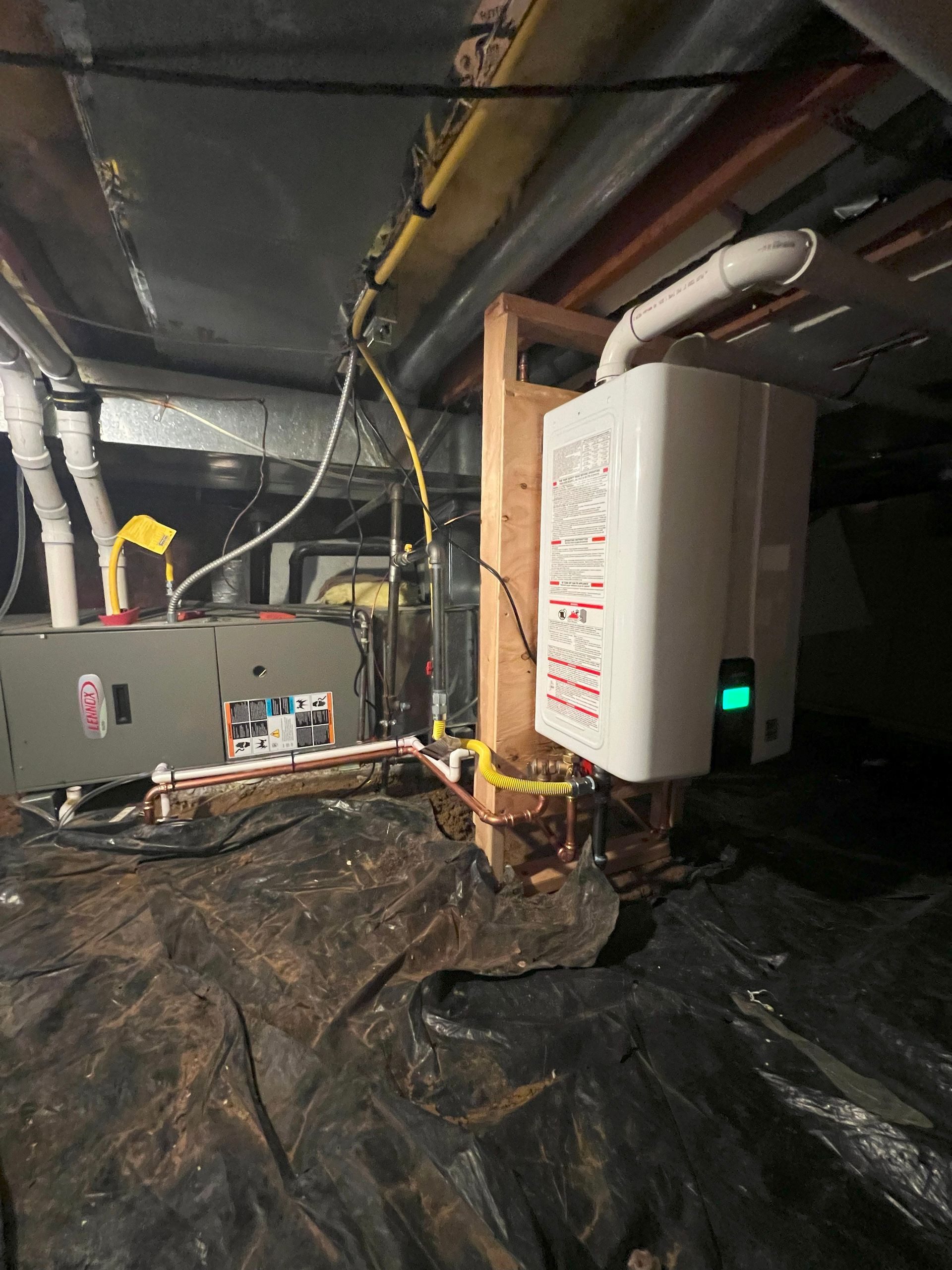 White tankless water heater mounted on a wood post in a basement. Furnace and pipes are also visible.
