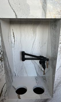 Recessed wall with marble effect, black adjustable faucet, and two round holes.