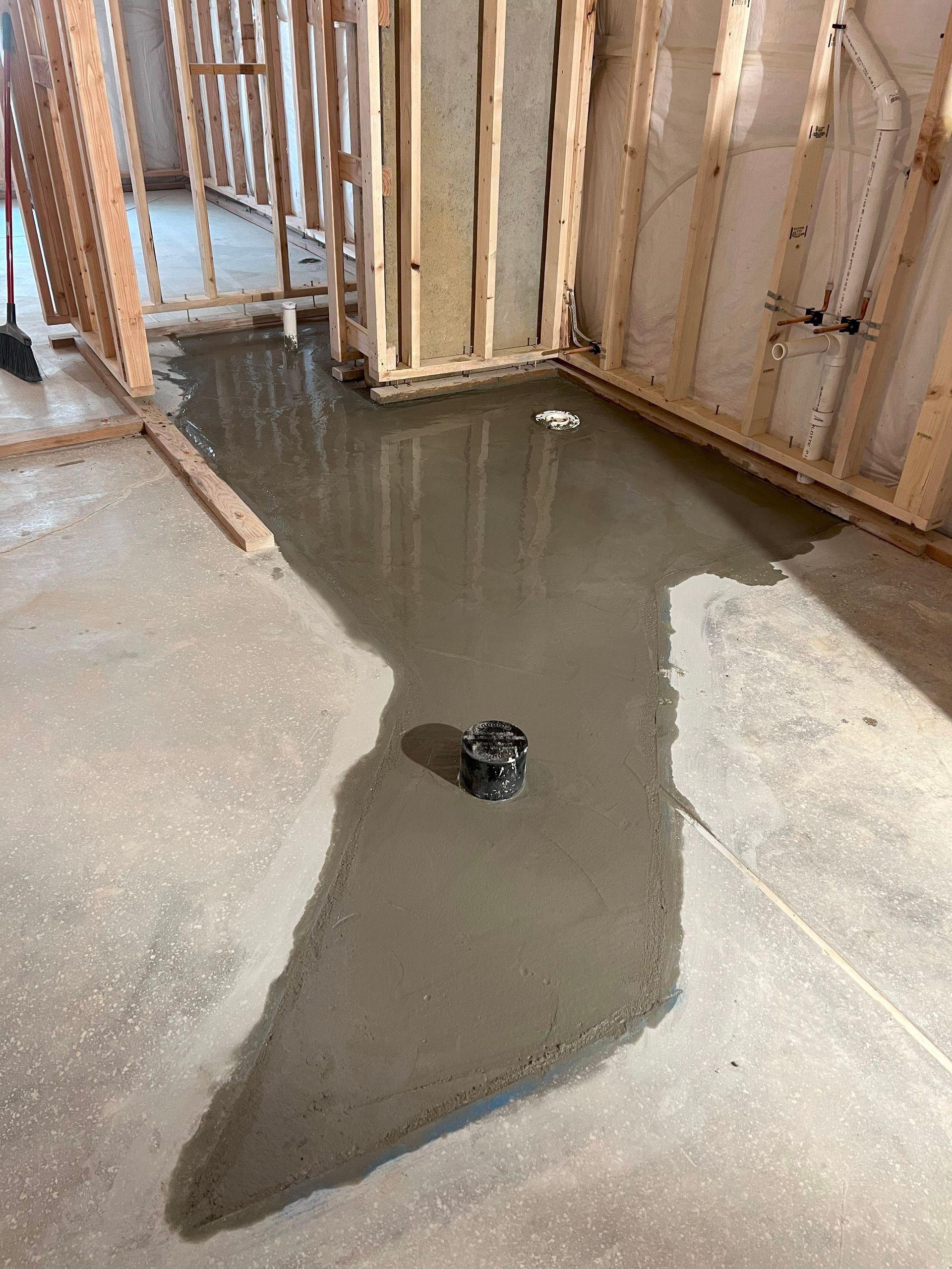 Concrete floor with a drain, inside of a building under construction; wooden framing visible.