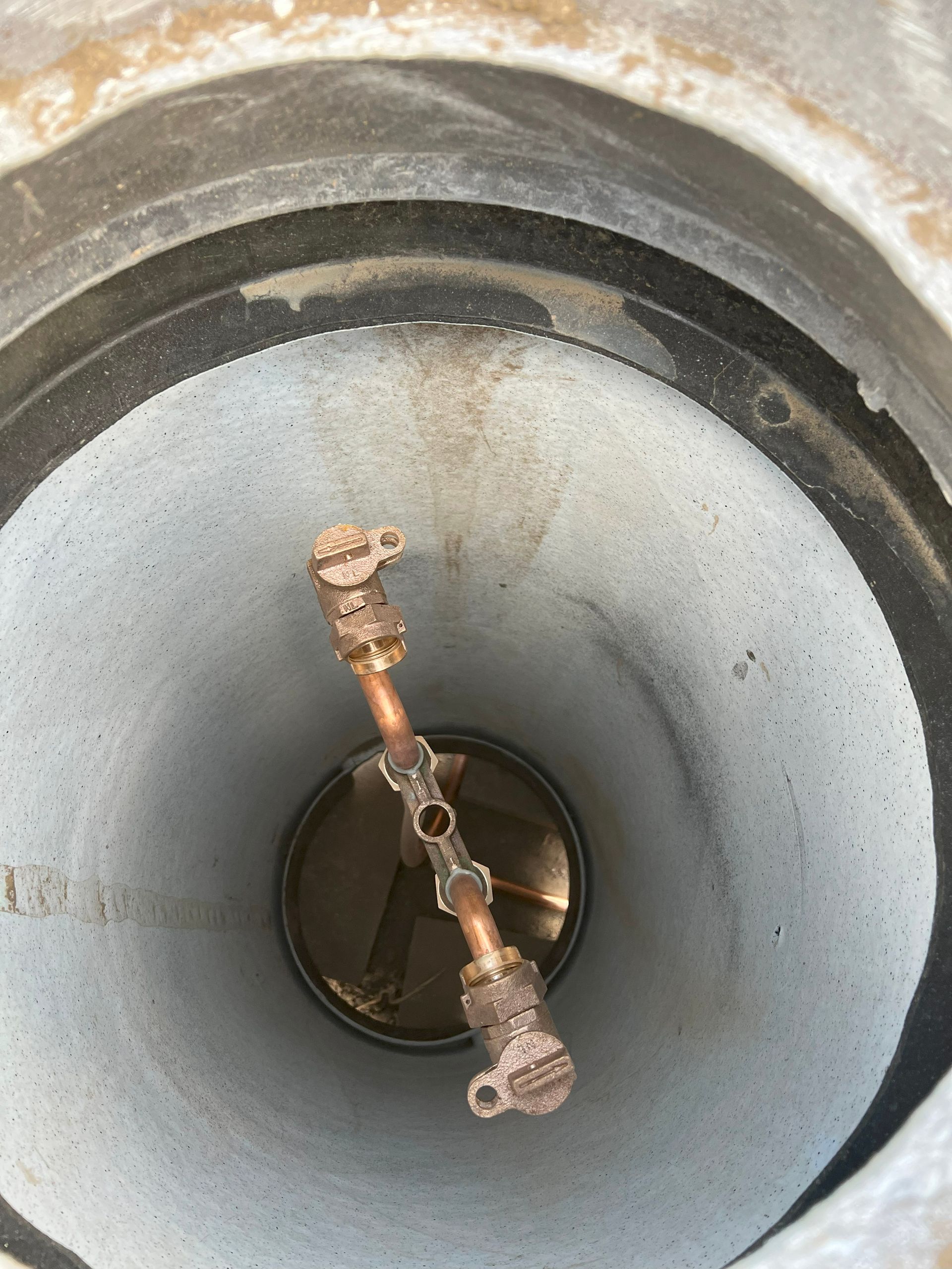 Copper pipe with valves inside a concrete cylindrical structure.
