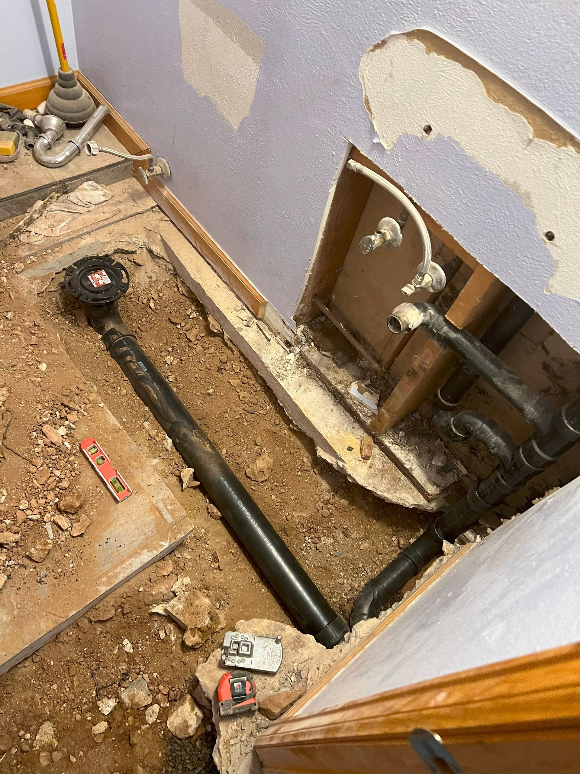 Plumbing work in progress. Black drain pipes, exposed wall and floor in a room.