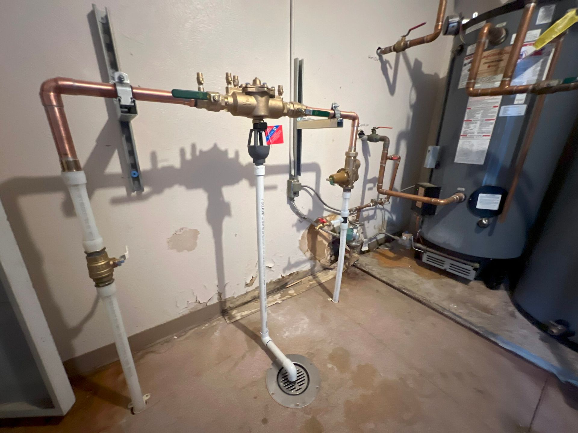 Plumbing system with copper pipes, a water meter, and a drainpipe connected to a floor drain in a basement.