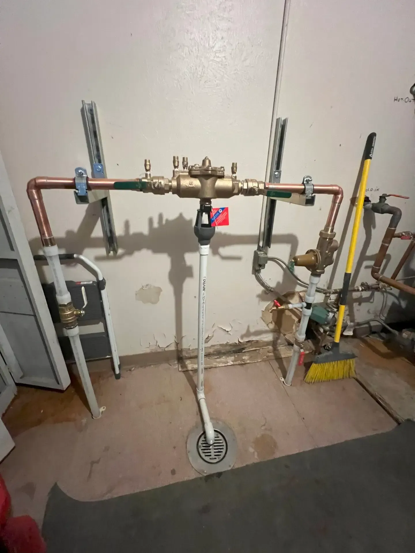Water supply pipes with a backflow preventer. Copper and brass pipes are mounted on a wall above a floor drain.