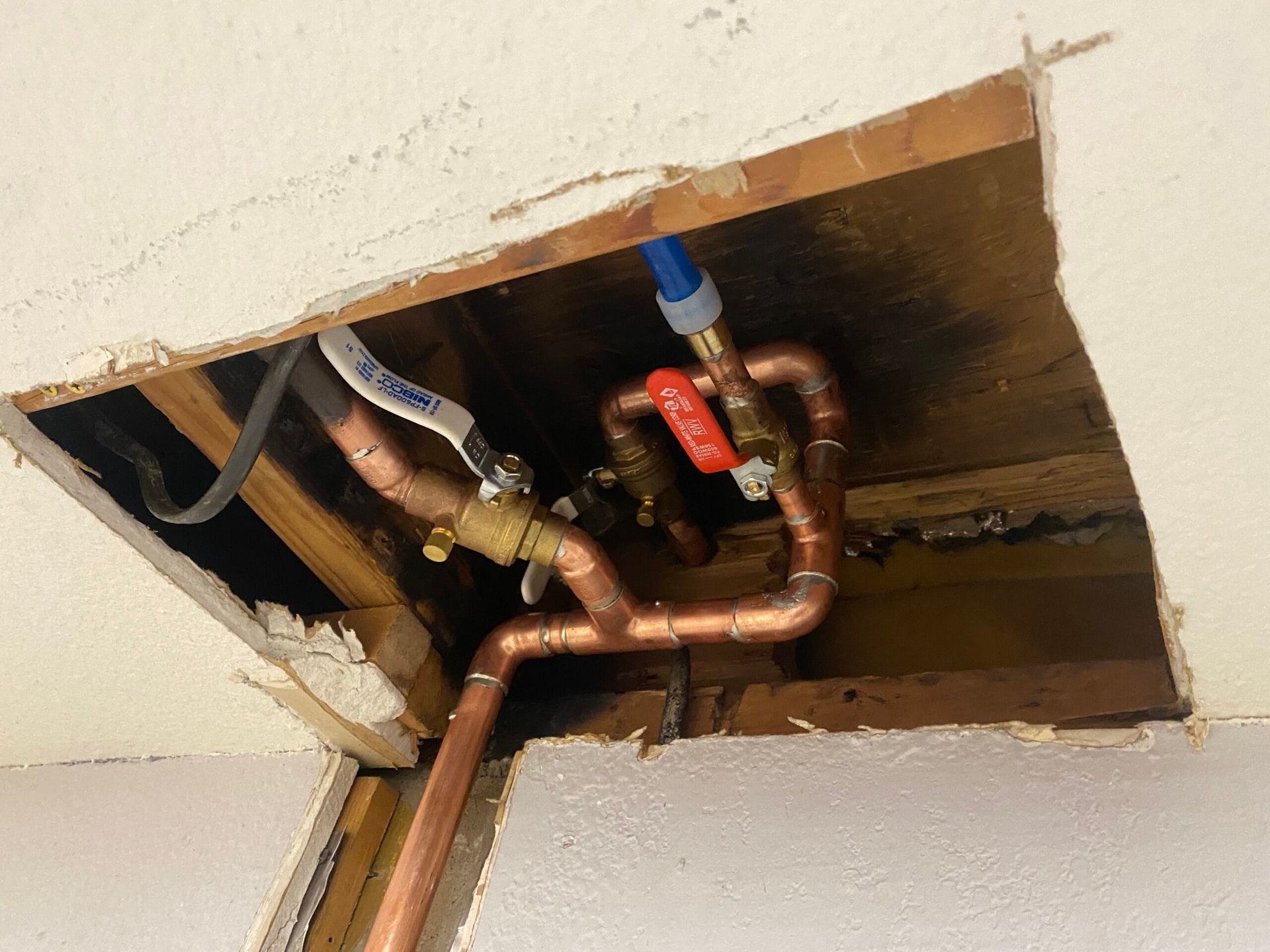 Copper plumbing pipes and valves in ceiling opening.