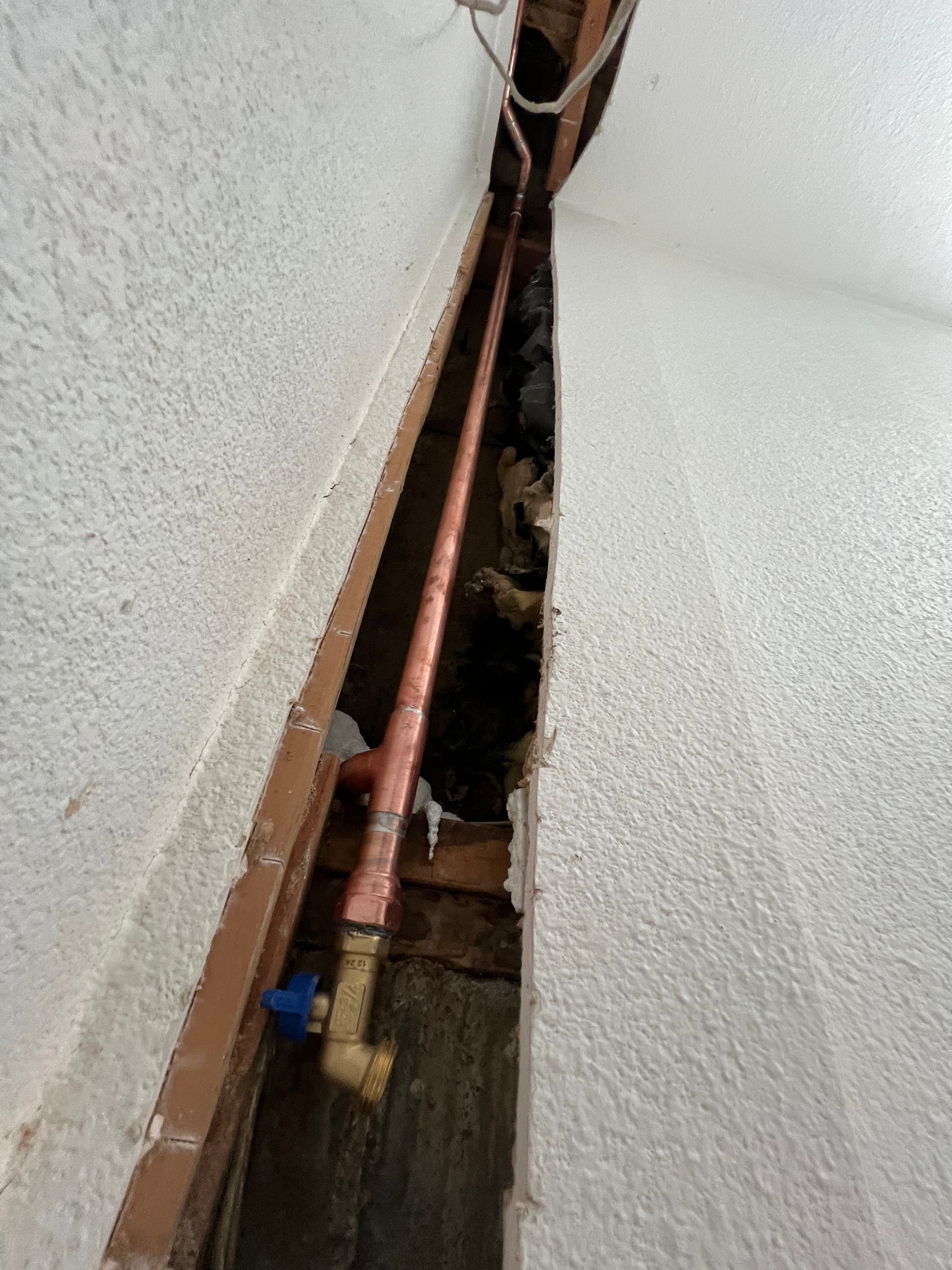Copper pipes and a blue valve exposed inside a wall.