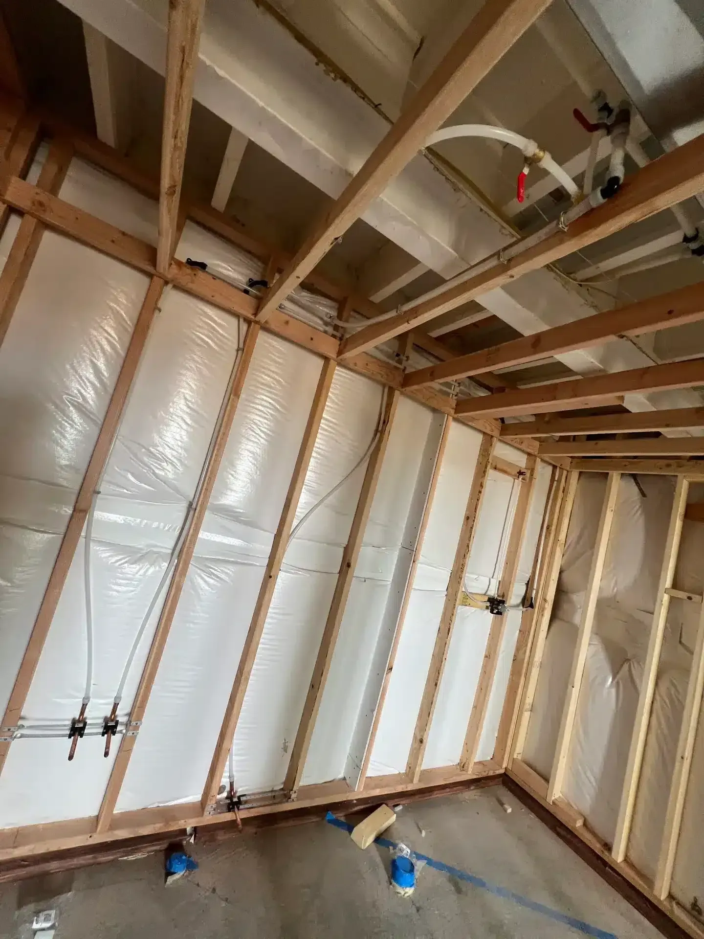 Interior of a room under construction with exposed wooden framing and insulation. Plumbing and wiring visible.