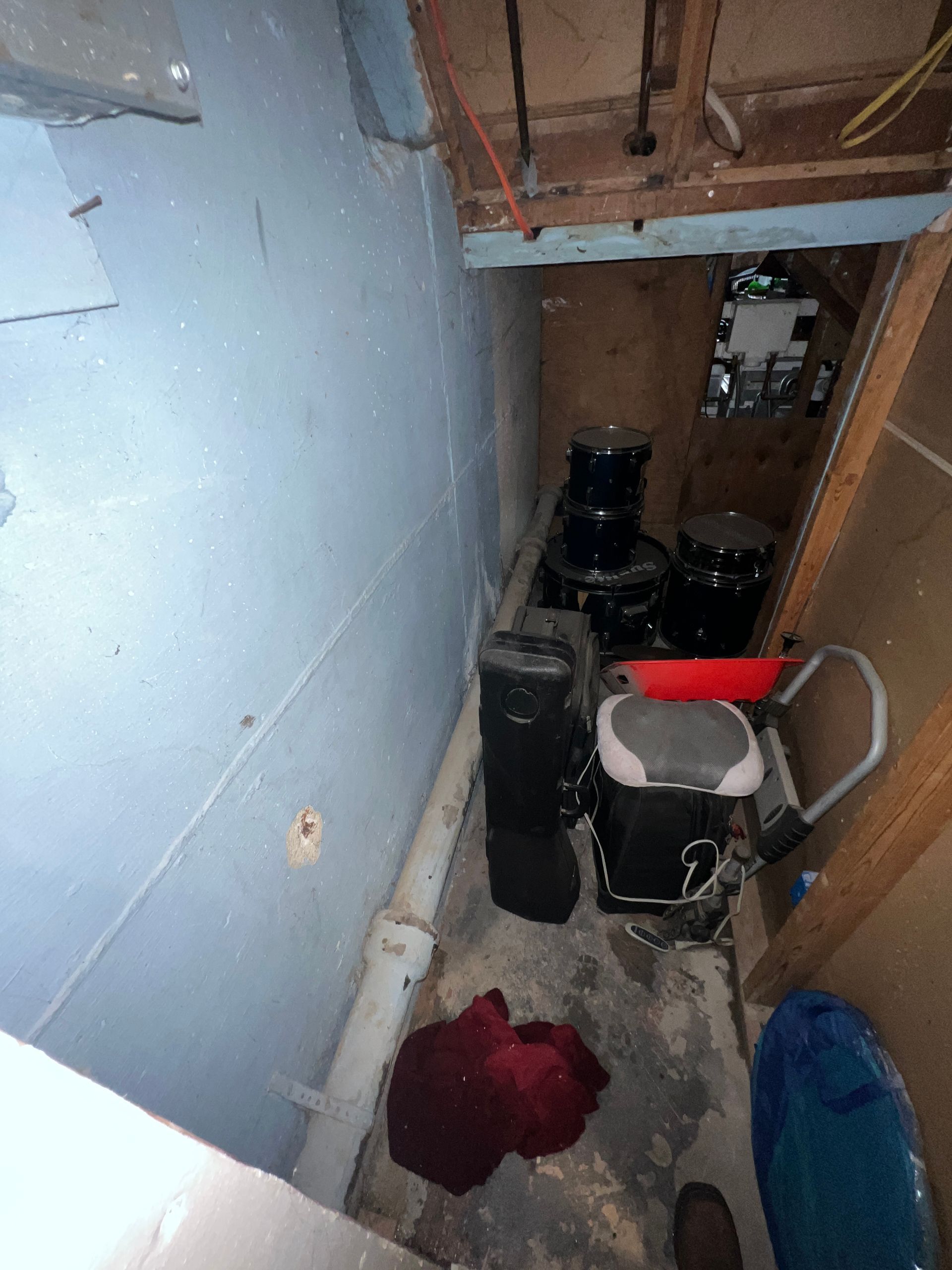 A narrow basement area with blue walls, appliances, and a red cloth on the floor.