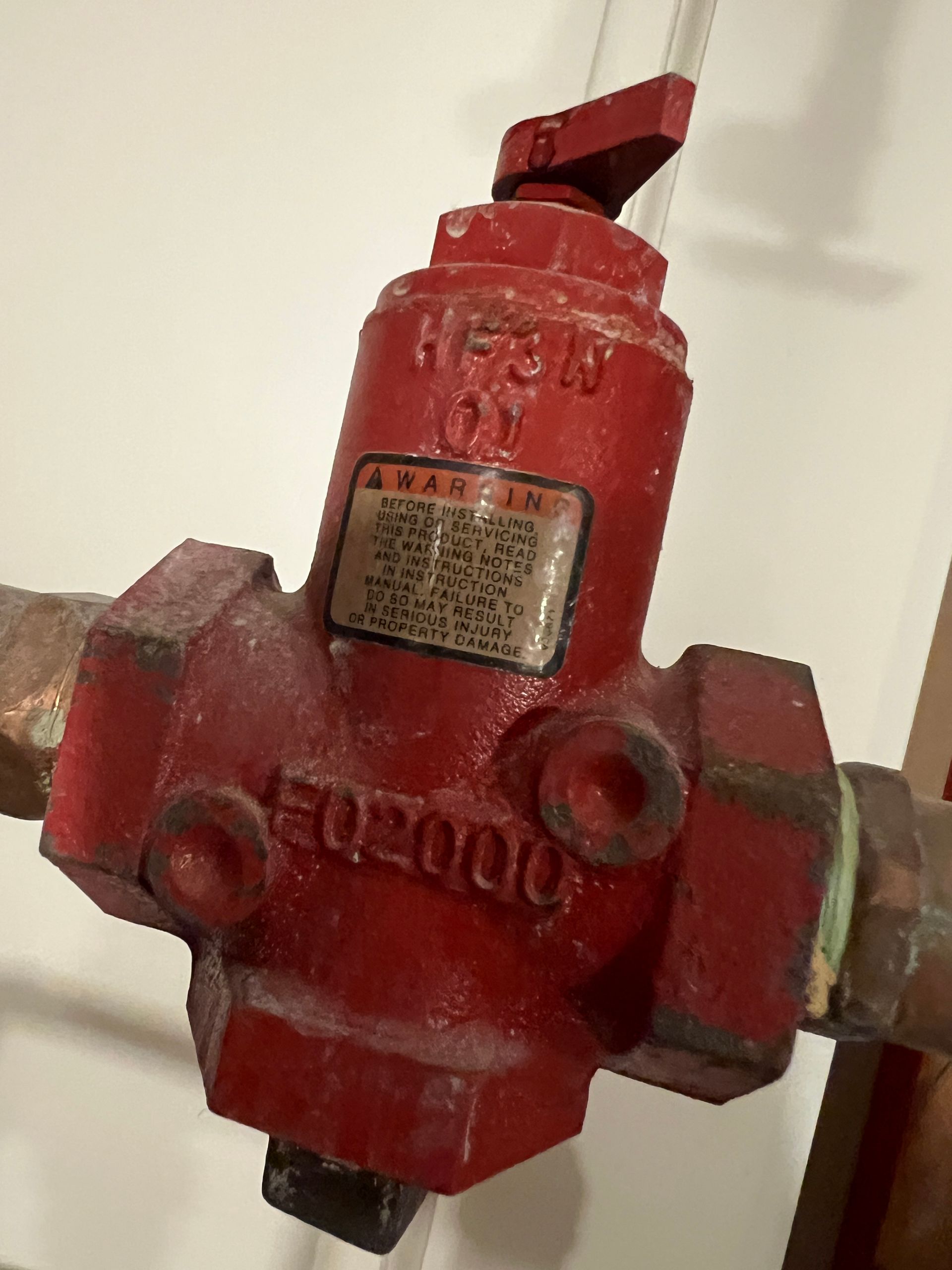 Red pressure reducing valve attached to pipes. It has a red handle and a label.