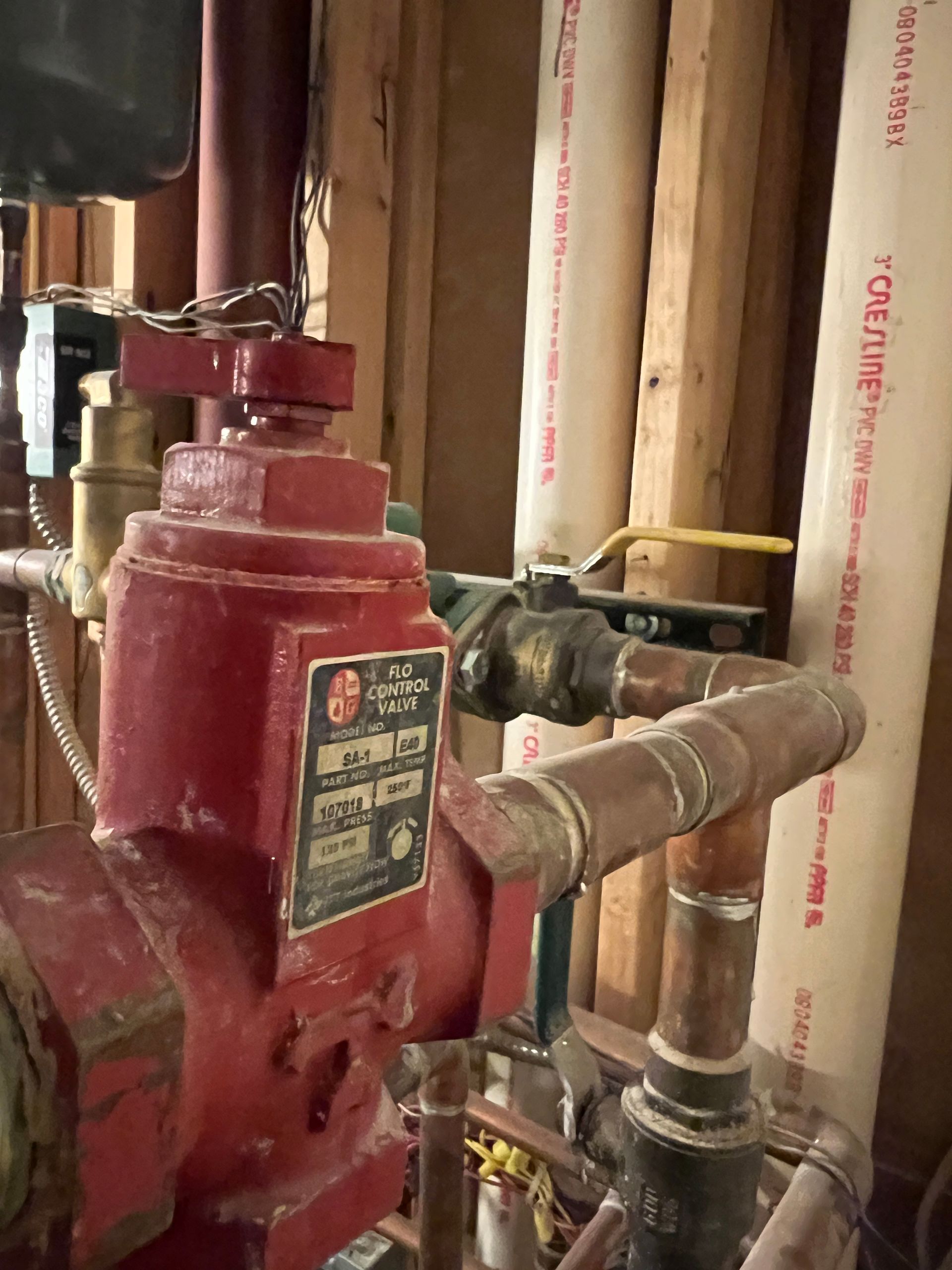 Red mechanical valve with attached copper pipes and a yellow-handled valve in a room with wood paneling.