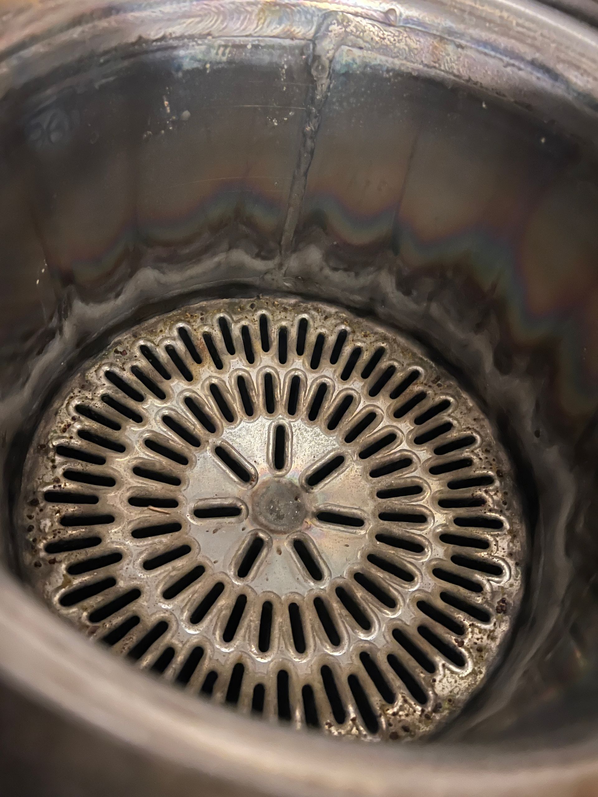 Inside of a stainless steel container with a circular, slotted grate at the bottom.