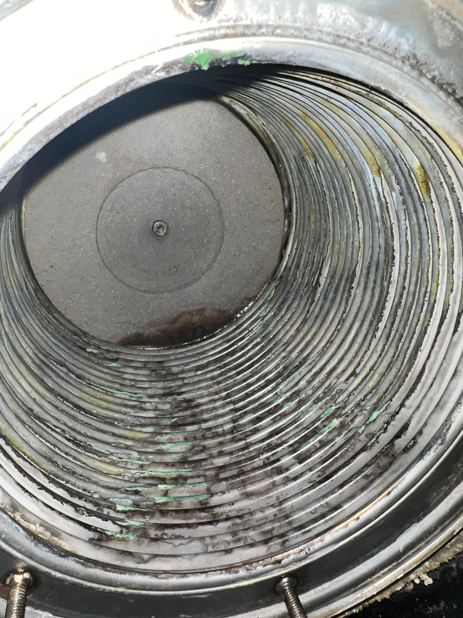 Inside view of a cylindrical industrial component with coiled, layered construction. Green and dark residue is visible.