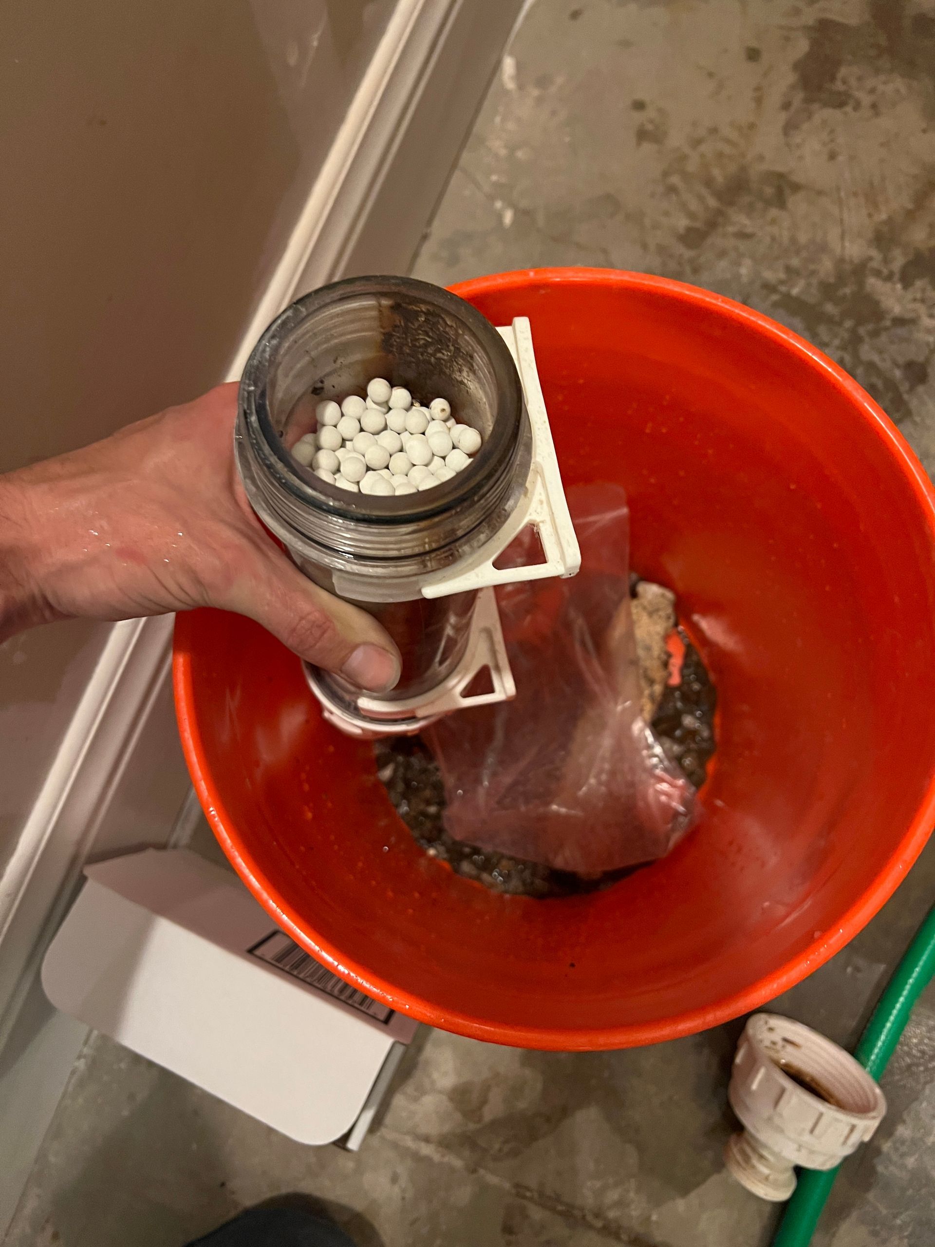 Hand holding jar with white balls above a red bucket containing a plastic bag and debris.