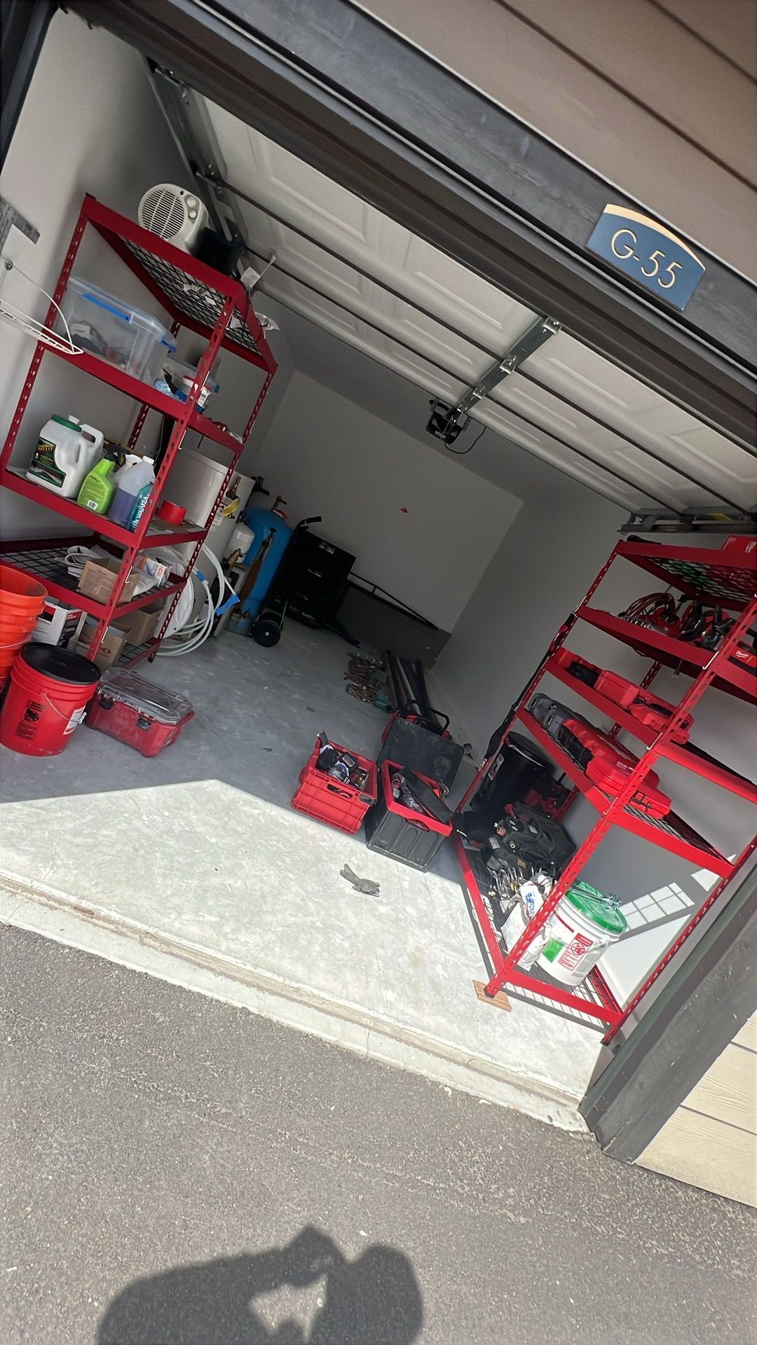 Garage interior with red shelving units, tools, and equipment. Garage door partially open.