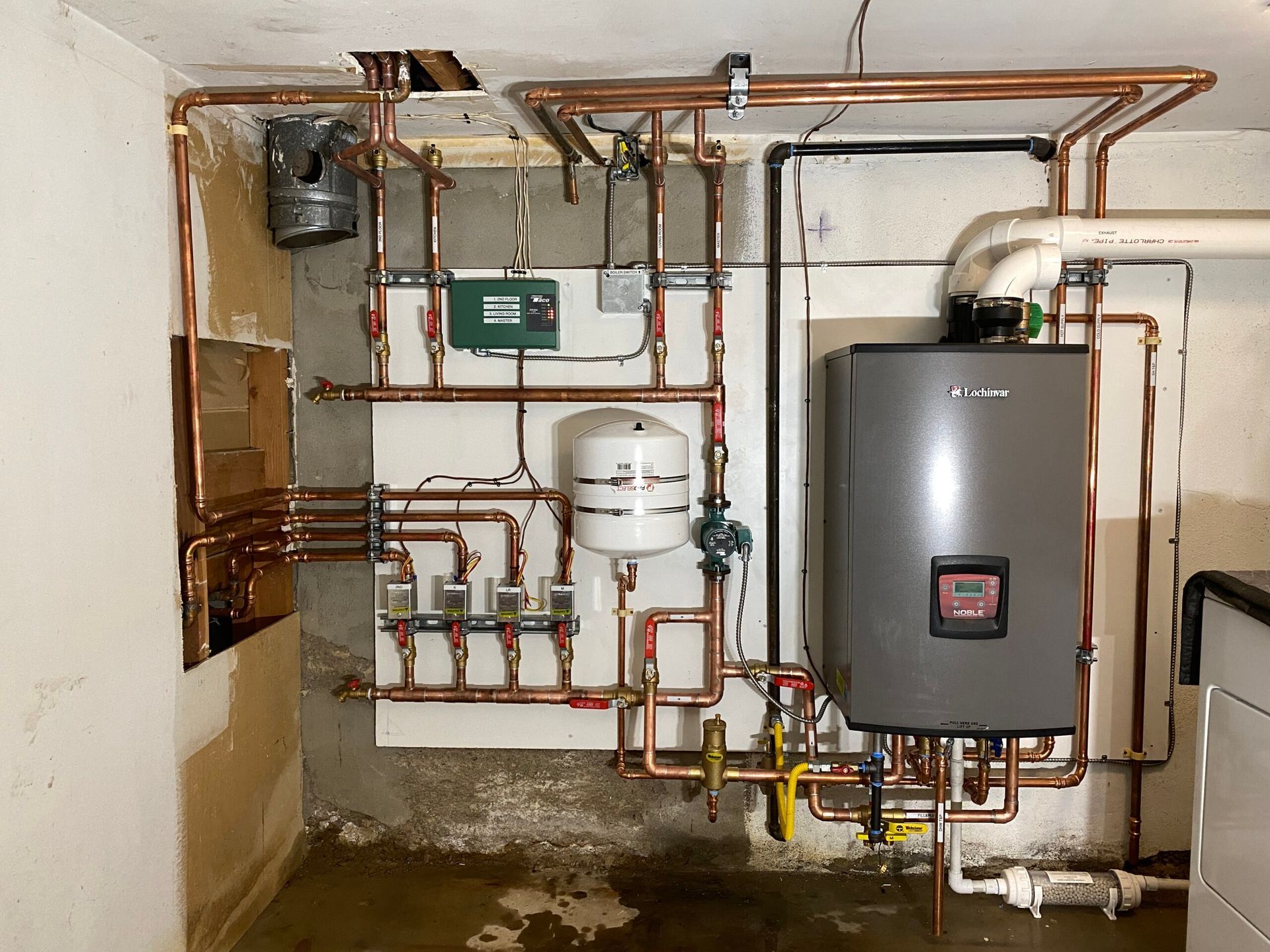 Copper pipes and a boiler system in a basement setting.