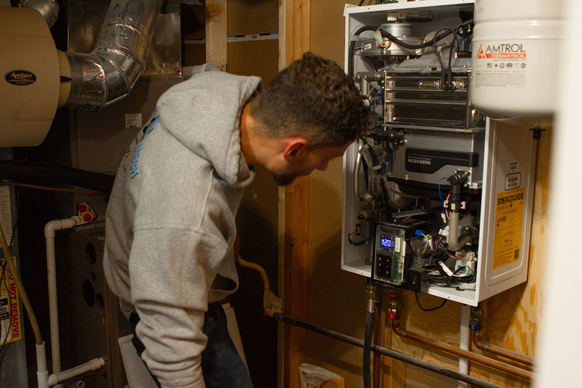 A person inspects a white appliance mounted on a wall in a room.