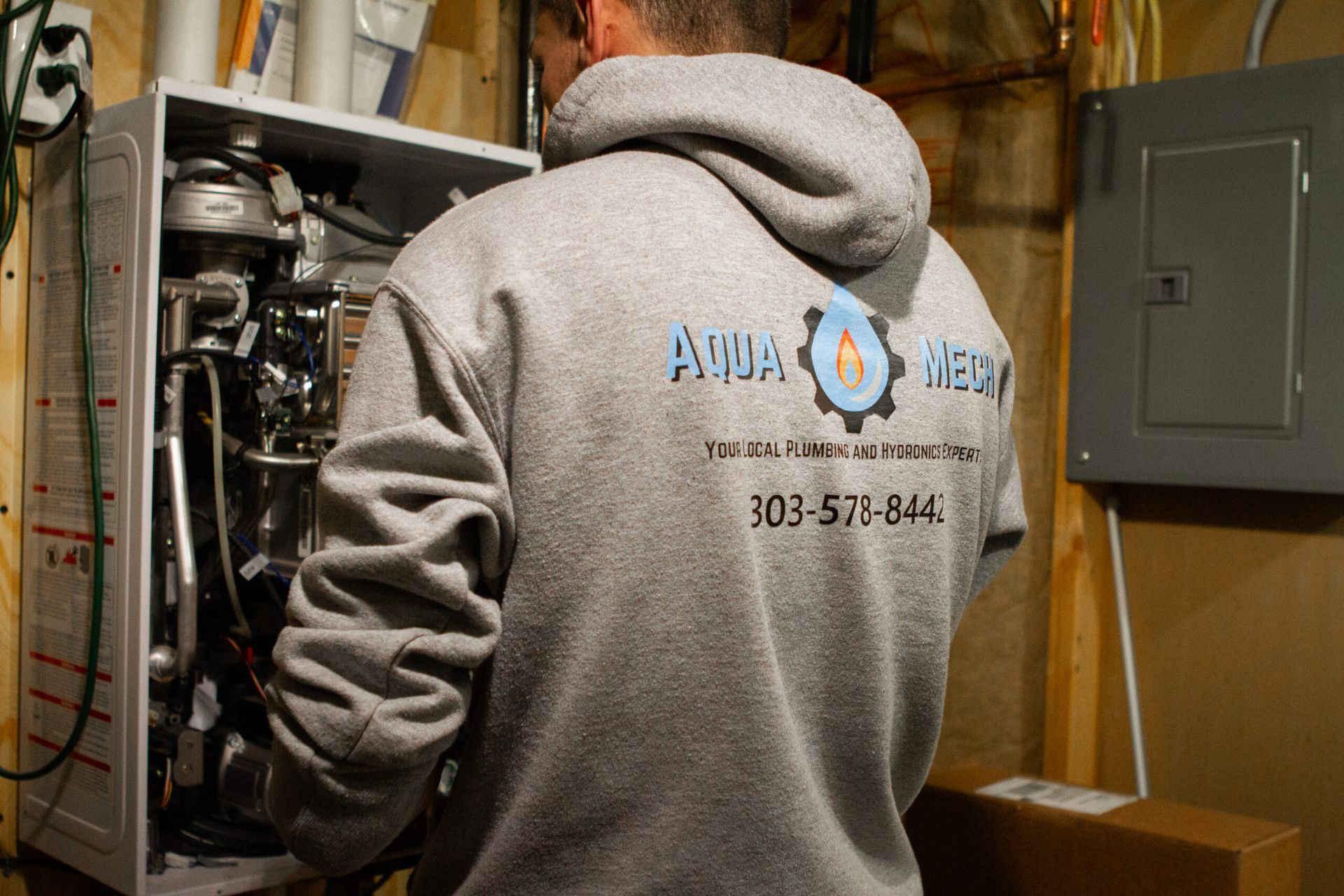 Man in gray hoodie working on a boiler, Aqua Medics logo visible.