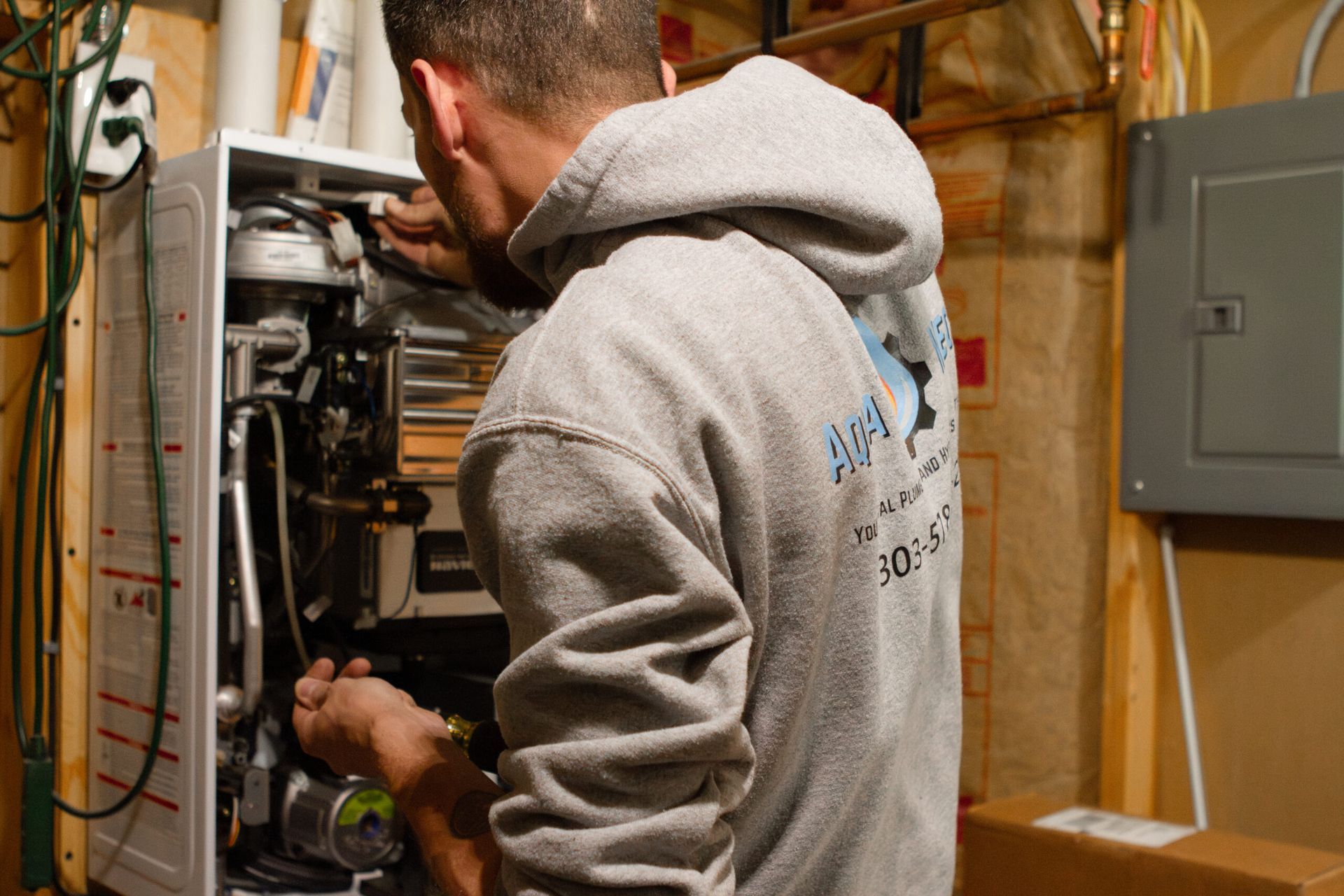 Man in gray hoodie working on a white heating unit in a basement.