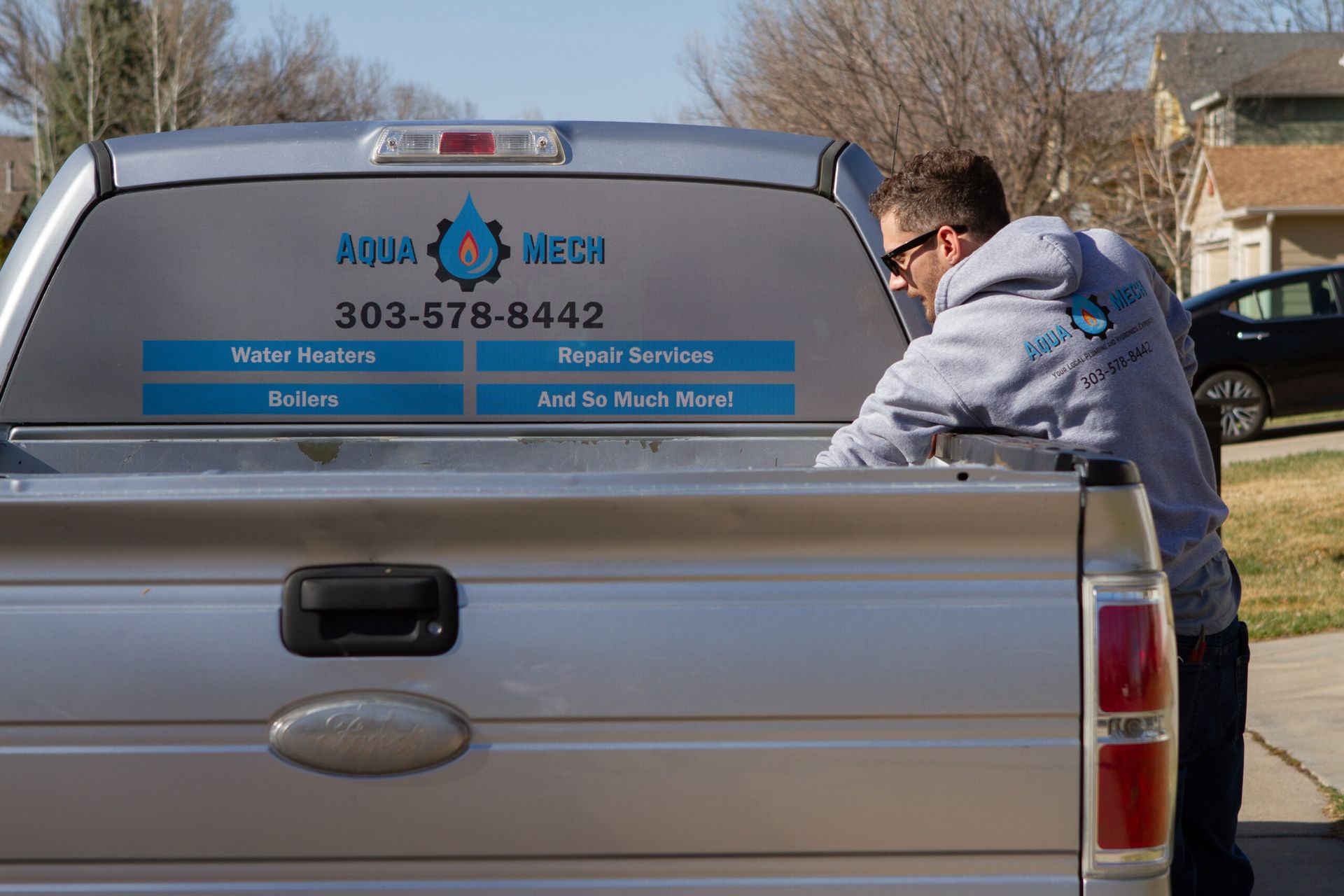 Man loading truck bed, back of Aqua Mech truck with logo and phone number.