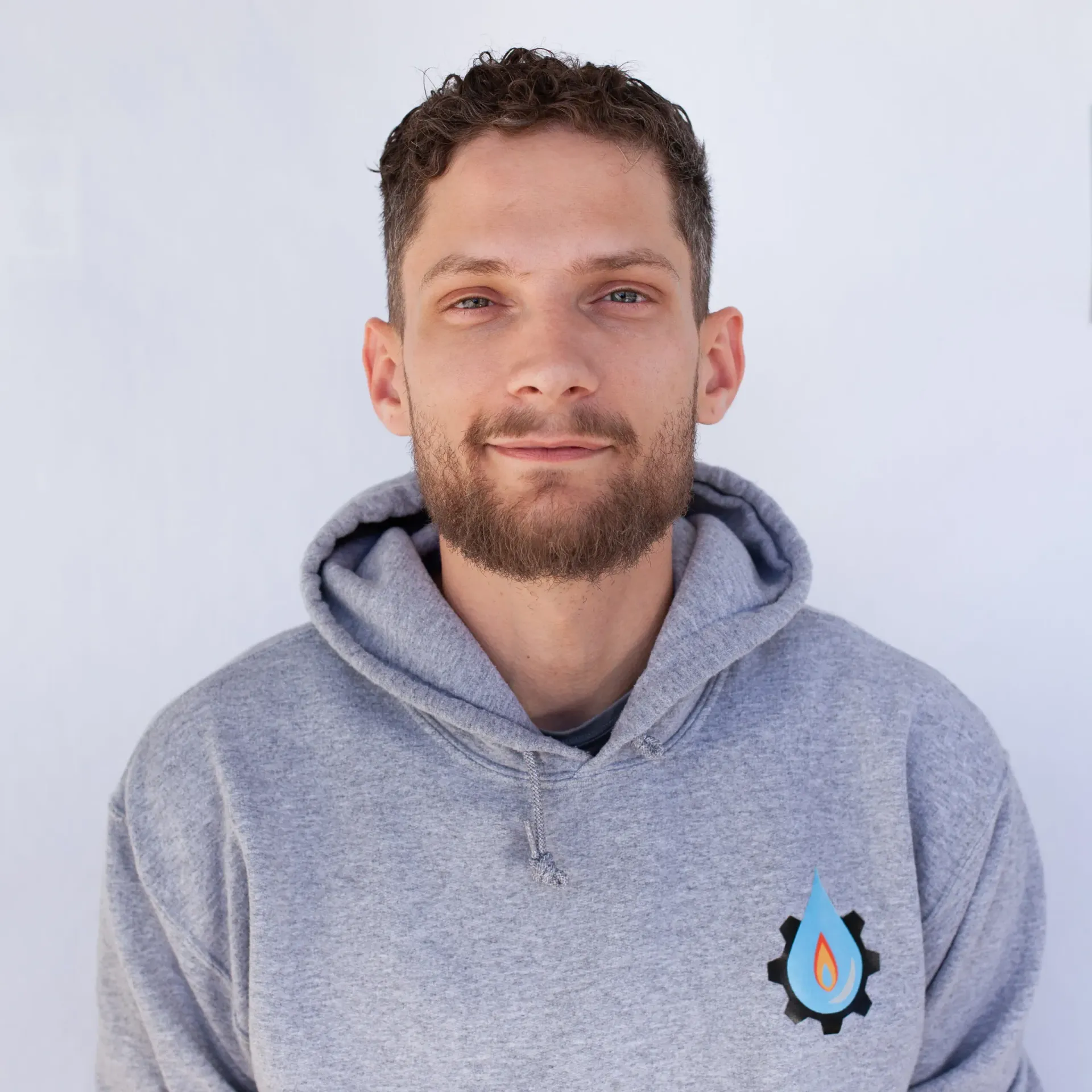 Man with curly hair and beard wearing a gray hoodie with a blue and orange logo.