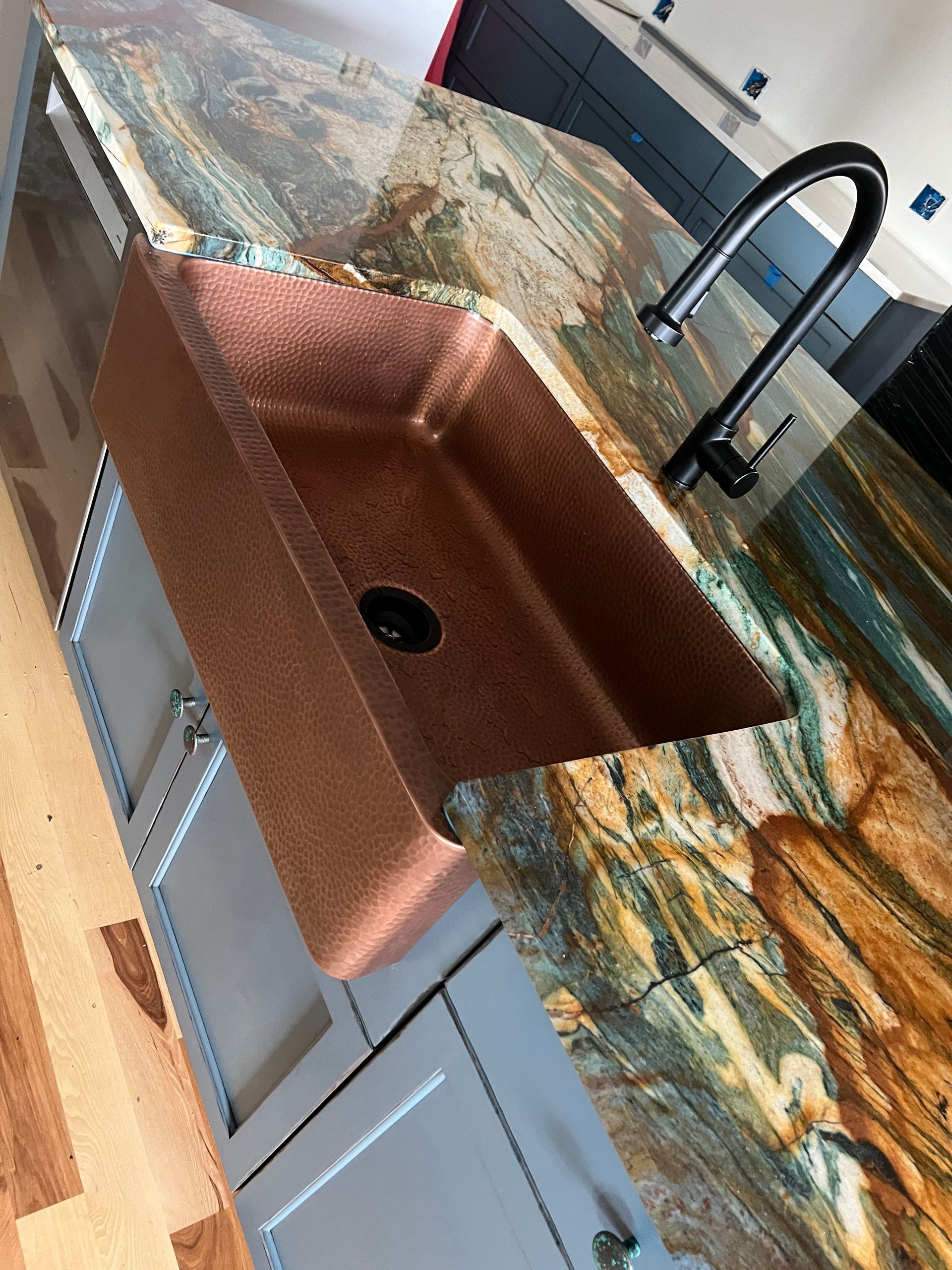 Copper sink in a granite countertop, with a black faucet; light blue cabinets below.