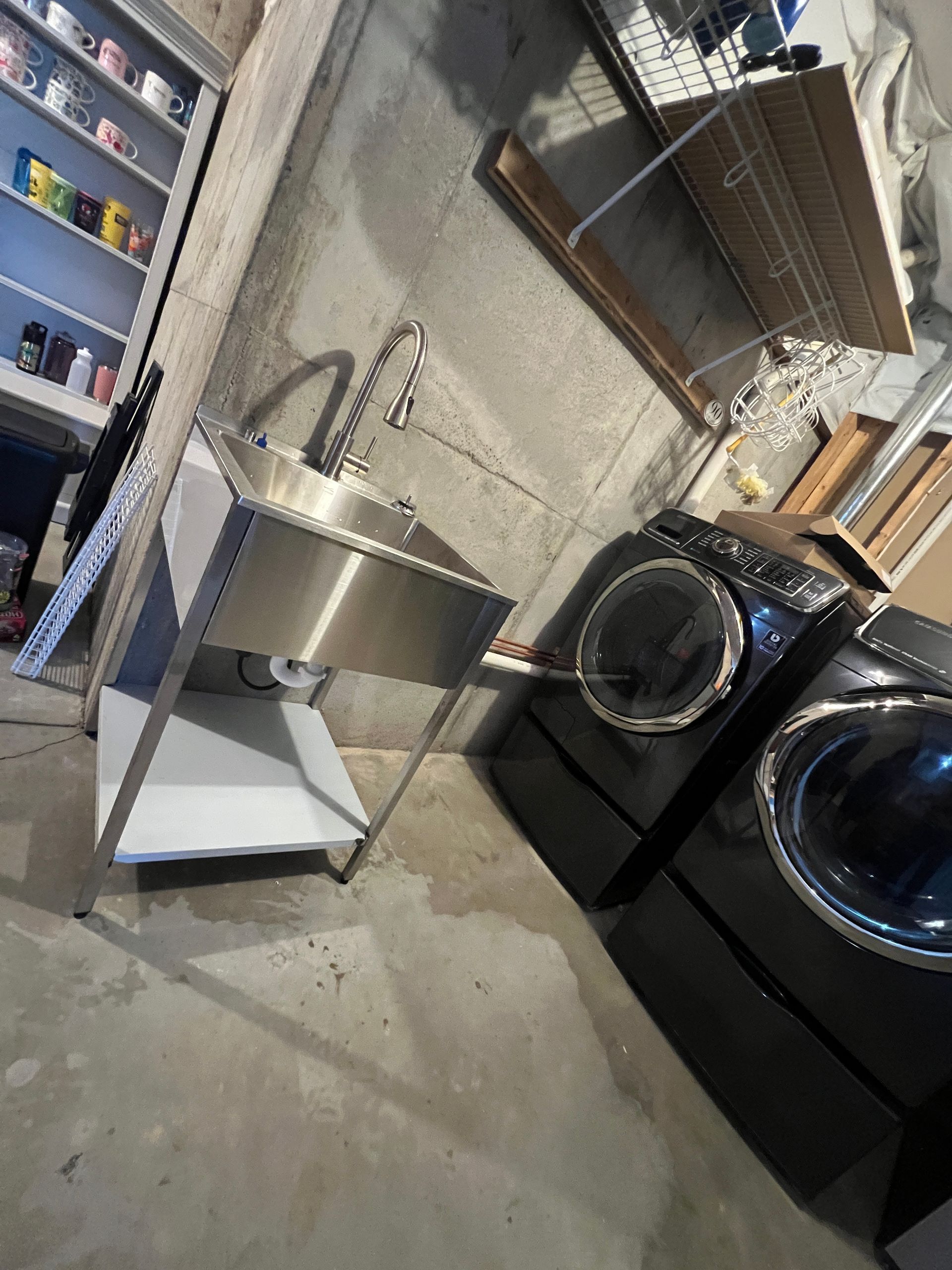 Stainless steel utility sink with faucet next to black washing machines in a basement.
