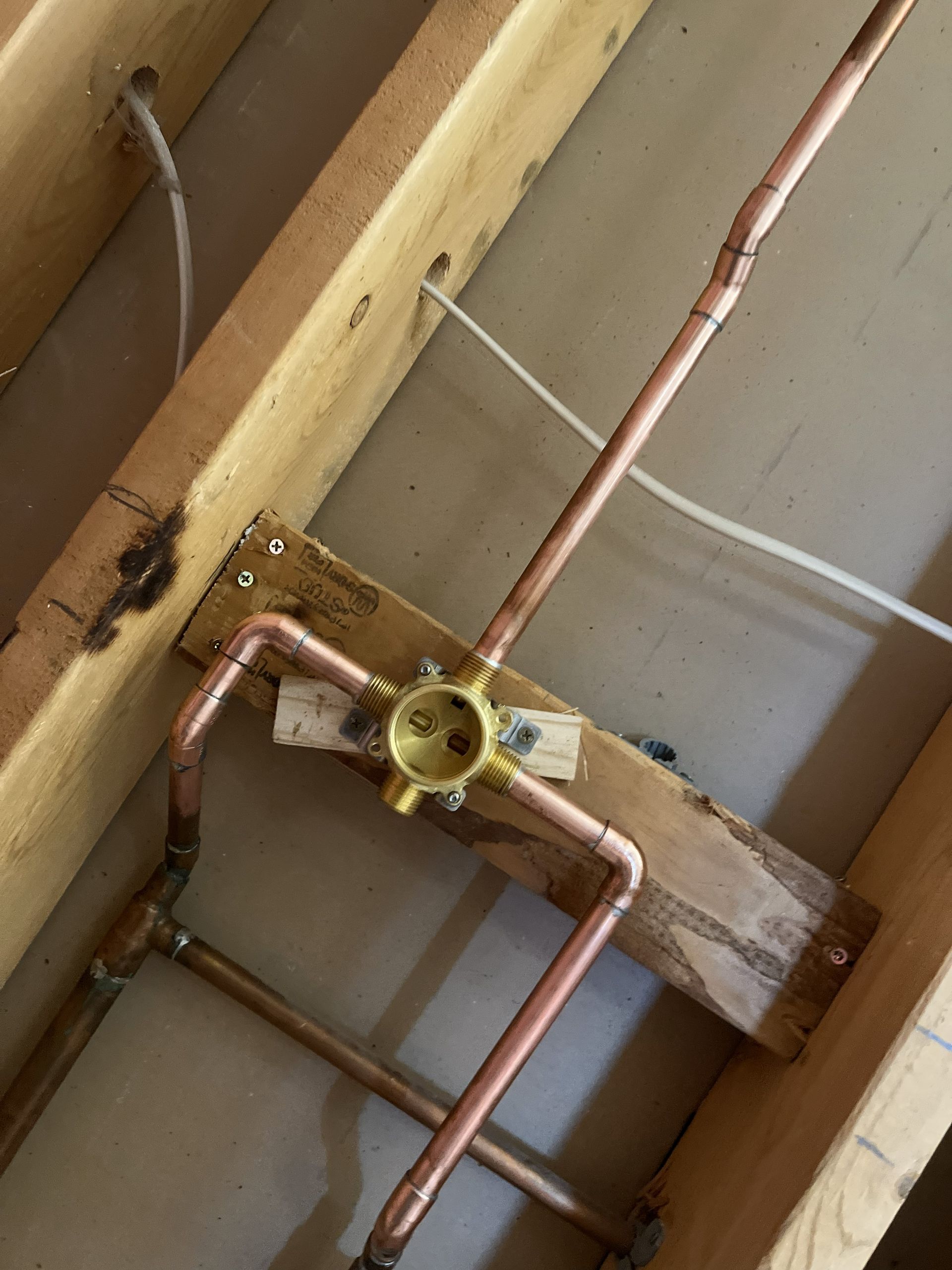 Copper pipes connected to a shower valve set within a wooden frame, viewed from below.