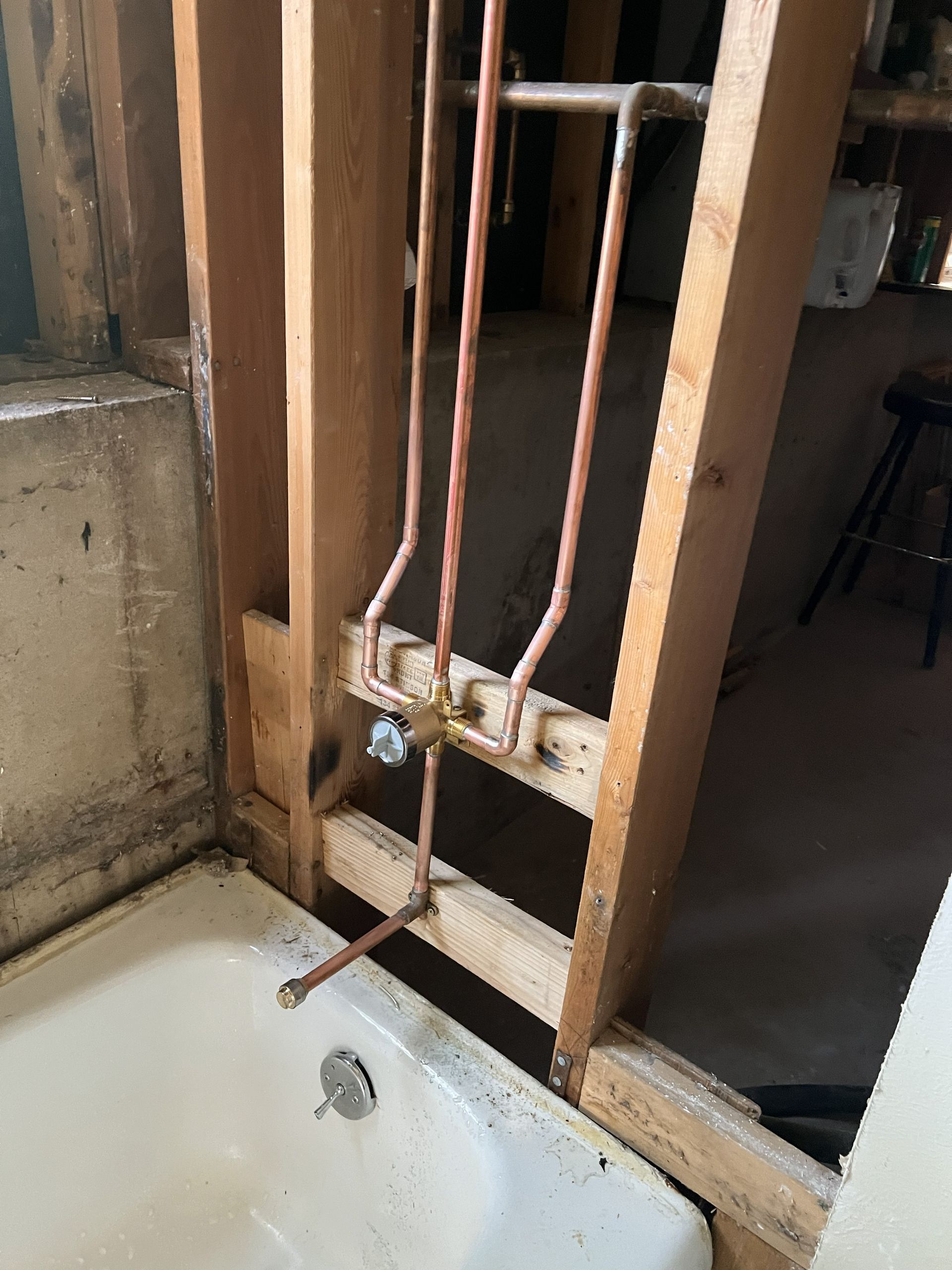 Copper plumbing pipes installed in a bathroom wall; tub below, unfinished studs visible.