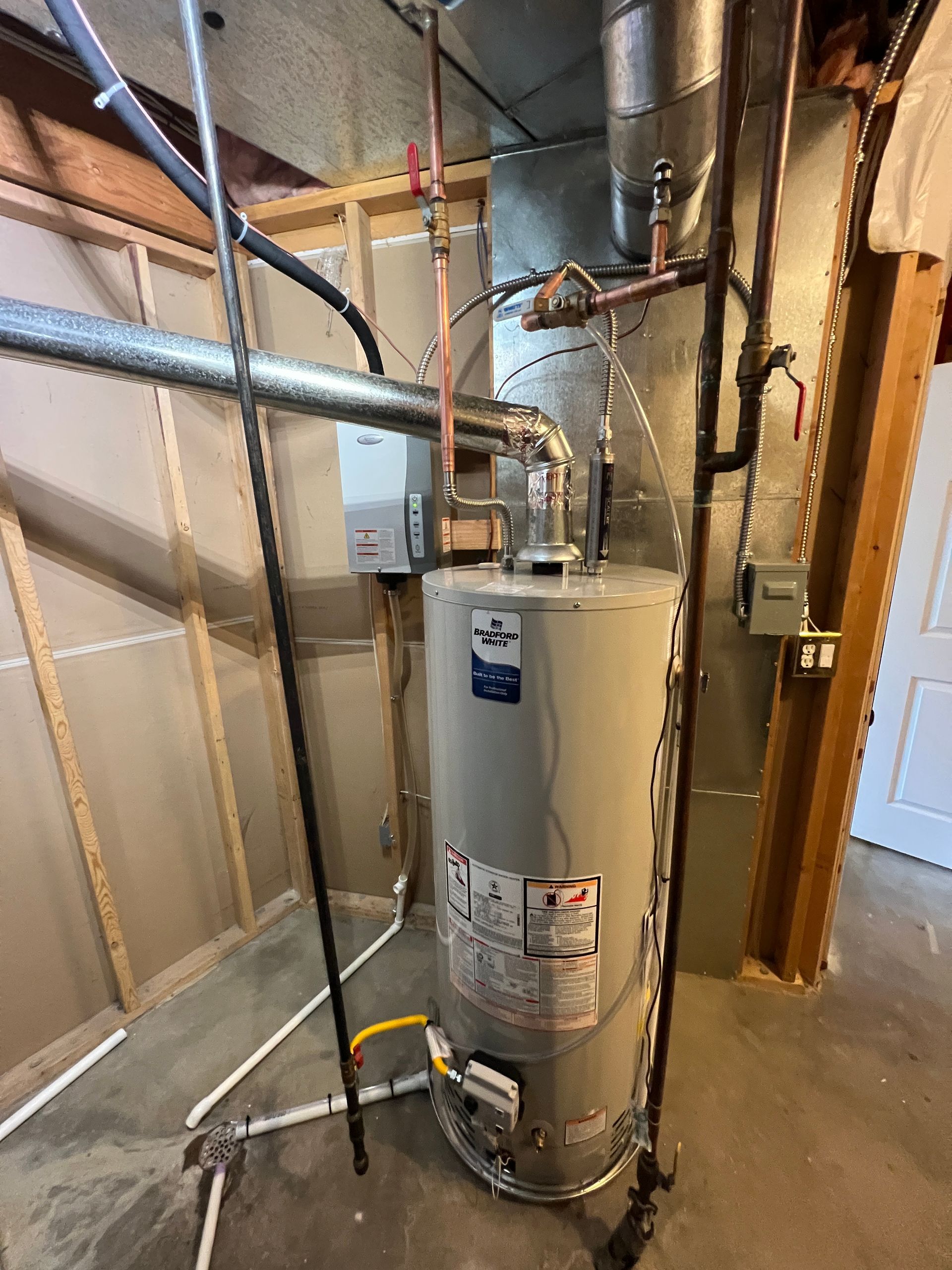 A water heater and tank in a utility room. Copper pipes and a gray vent pipe are visible.