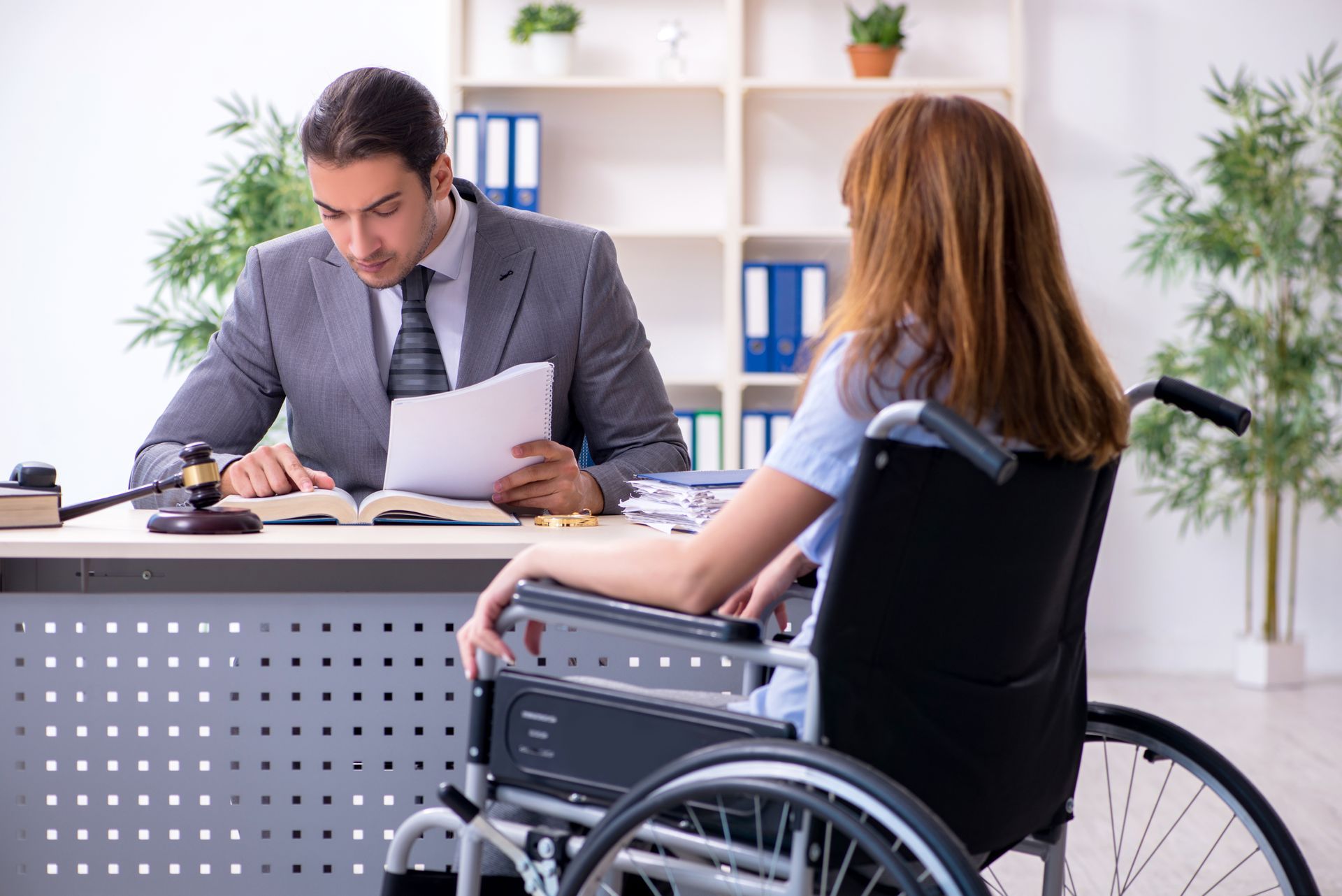 The backside of an injured woman in a wheelchair and a male lawyer in an office.
