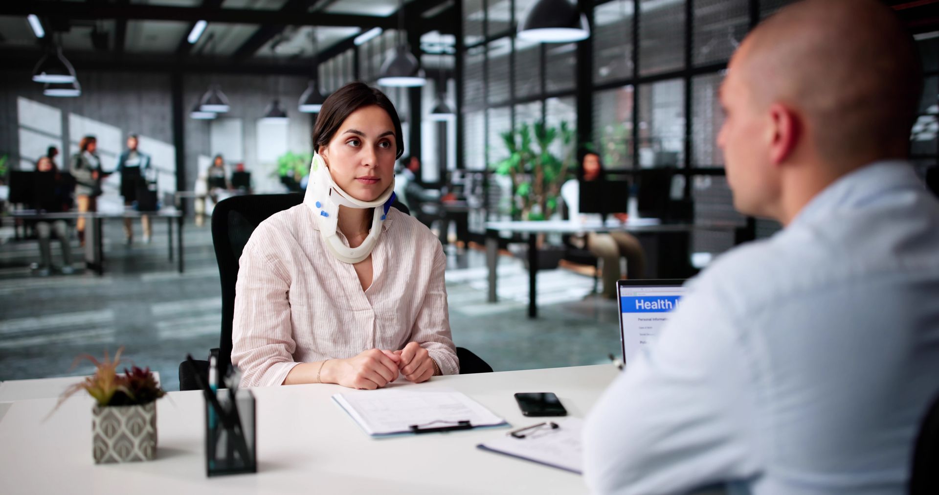A woman with a neck brace speaks to a worker compensation lawyer, inside an office.