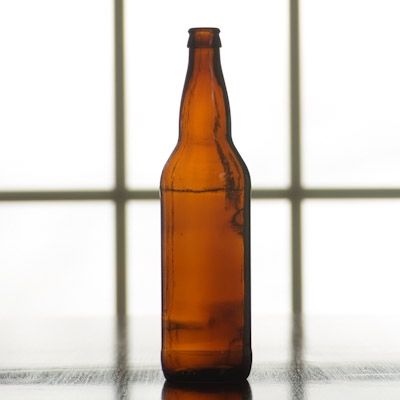 An empty beer bottle sits on a table in front of a window