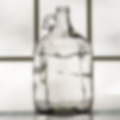 An empty glass bottle with a handle is sitting on a table.