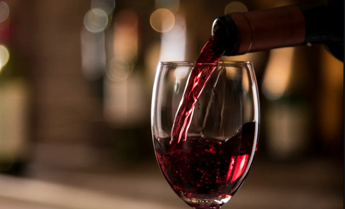A glass of red wine is being poured from a bottle.