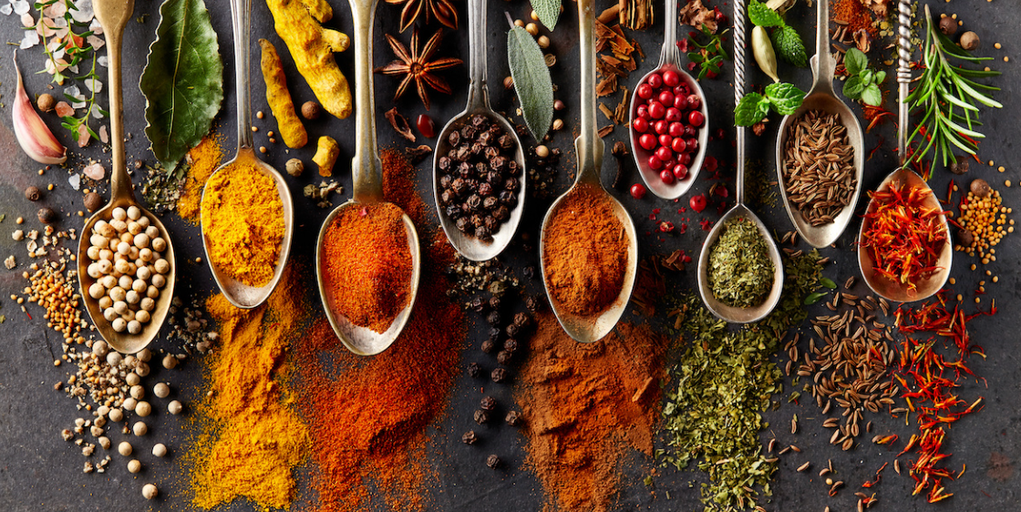 A variety of spices and herbs in spoons on a table.