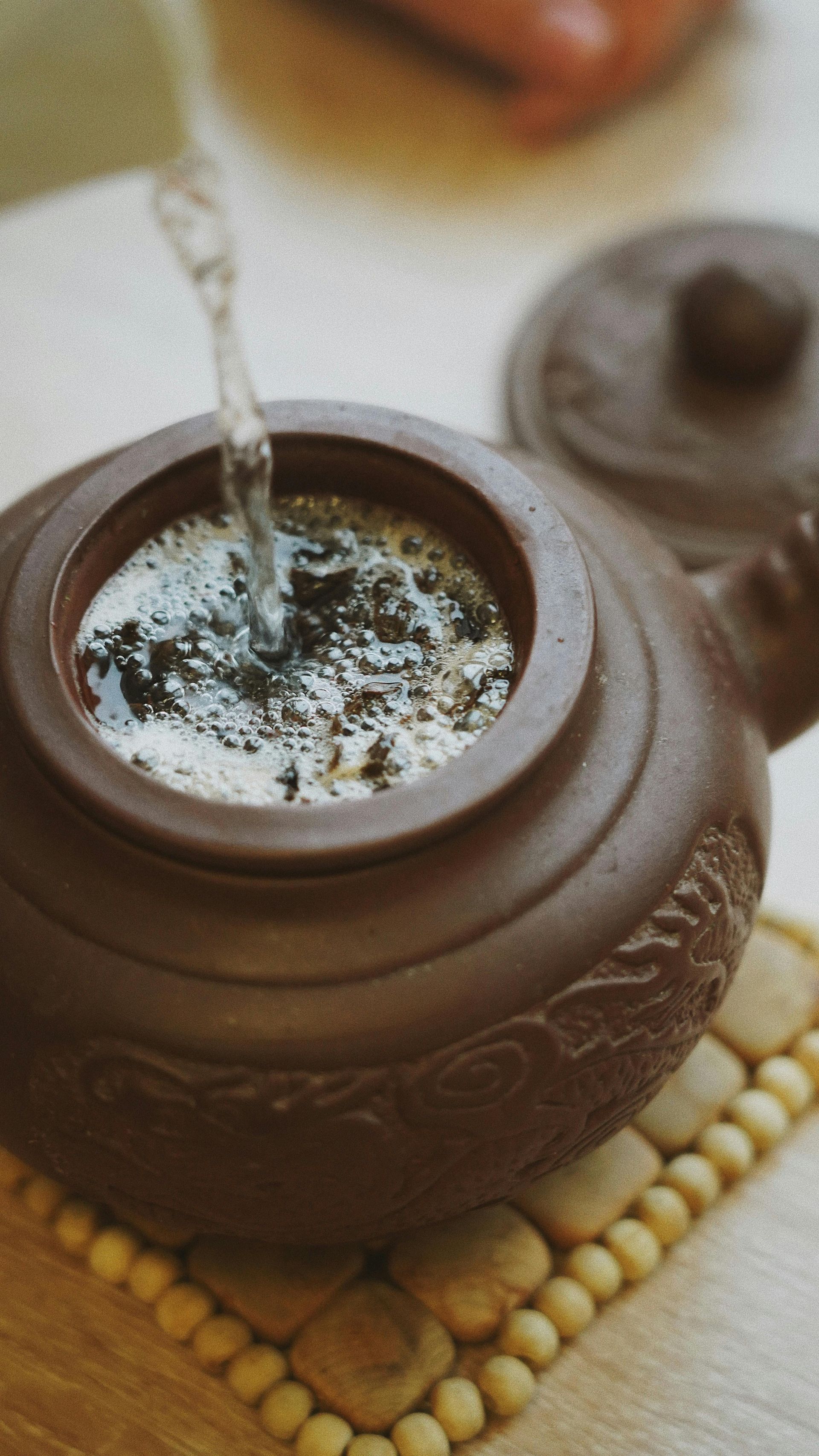 A person is pouring water into a teapot on a table.