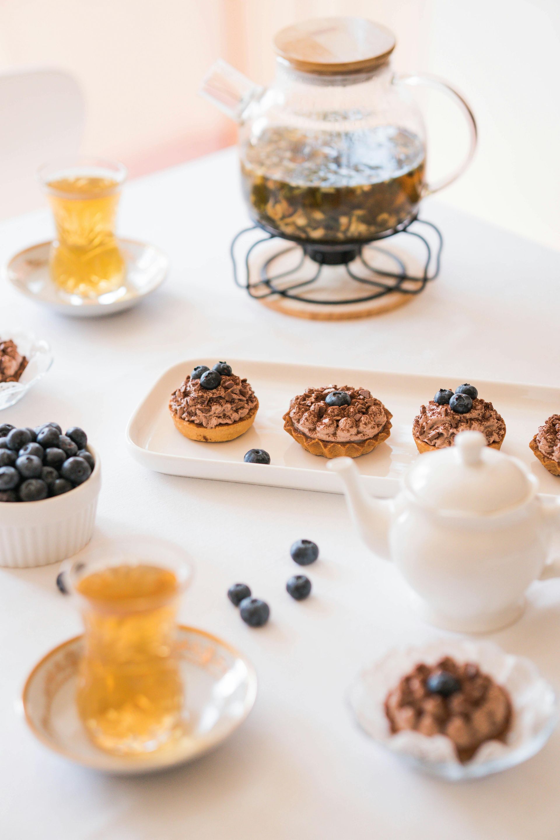 A table topped with cupcakes , blueberries , tea and a teapot.