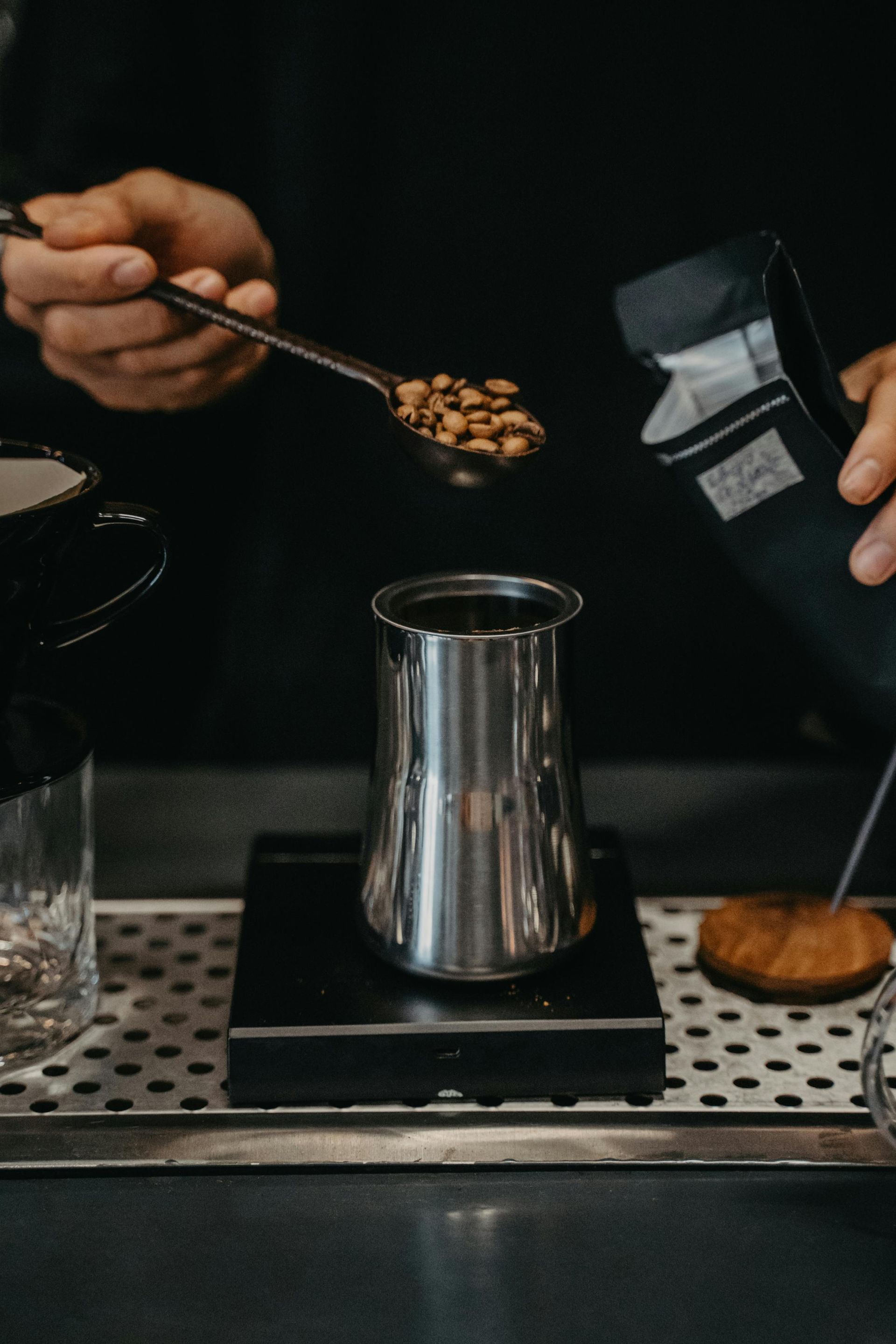 A person is pouring coffee beans into a pitcher with a spoon.