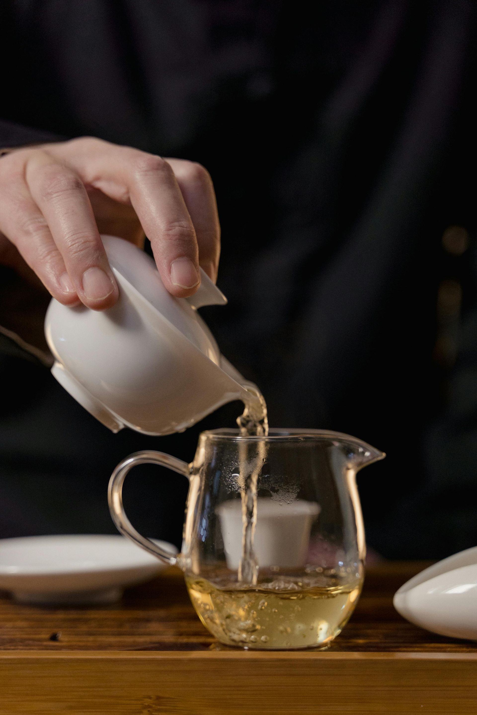 A person is pouring tea from a pitcher into a glass cup.