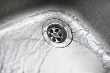 Close-up of a metal sink drain with water droplets on a gray basin surface