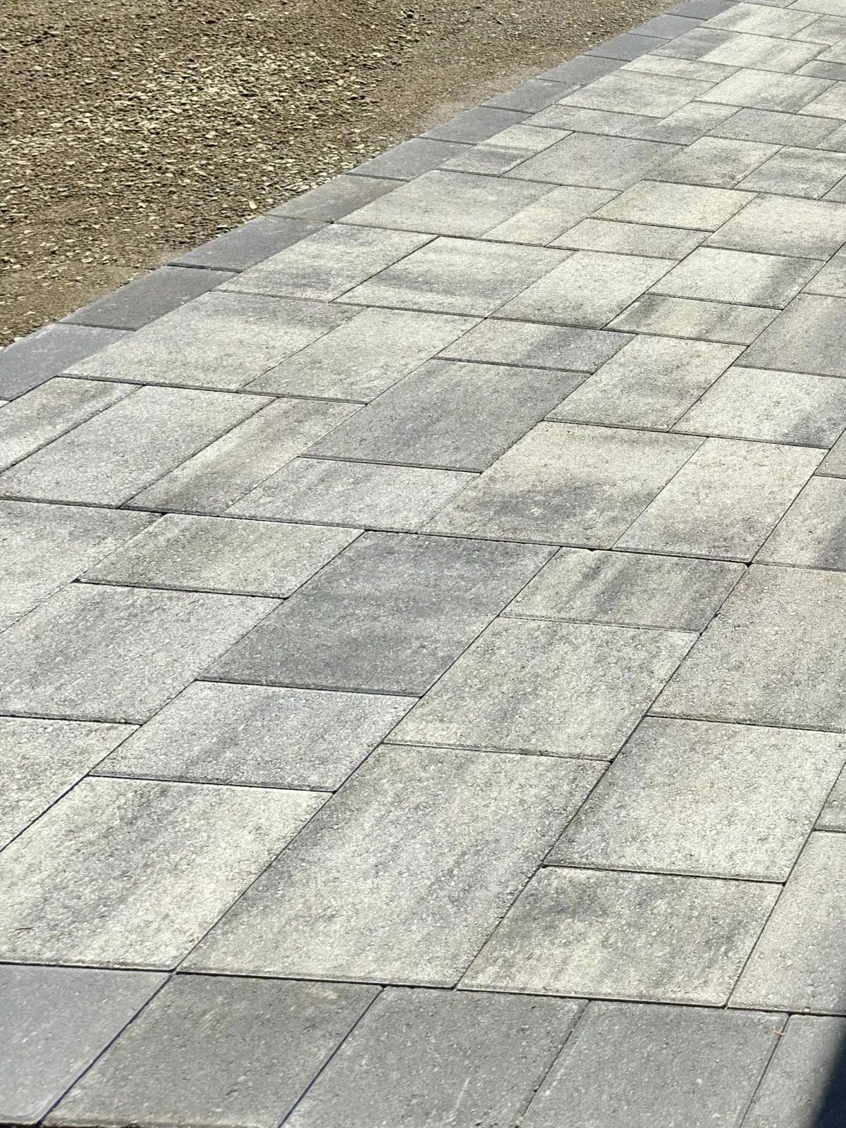 Gray stone-paved walkway beside a gravel path, viewed at an angle