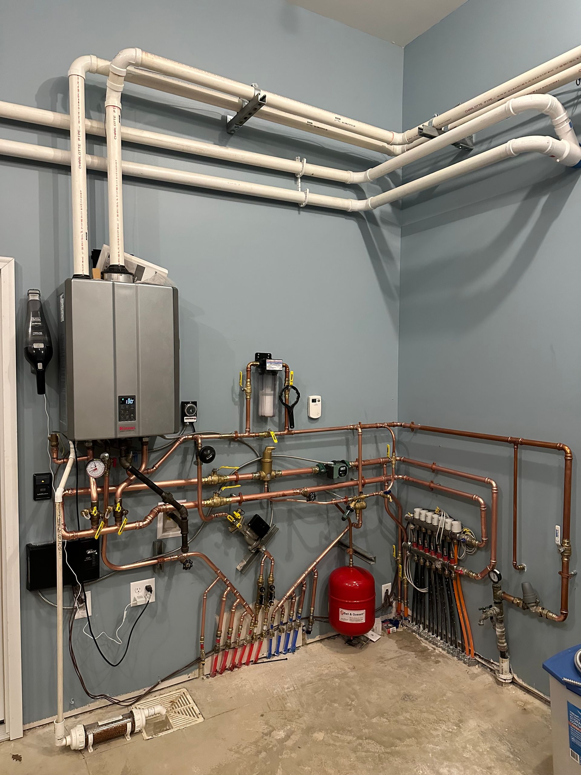 A room with a lot of pipes and a boiler on the wall.