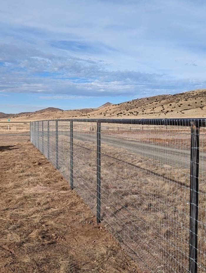 Wire fence running through a dry desert landscape under a cloudy blue sky.