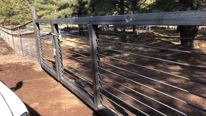 Metal ranch gate with horizontal wires beside a dirt road and trees in a wooded area