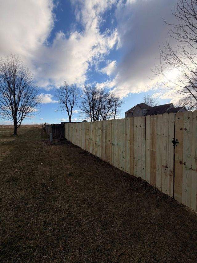 Backyard with a wooden fence, leafless trees, and a cloudy sky at dusk