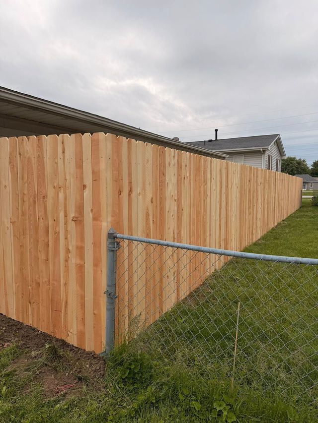 Wooden privacy fence along a grassy yard under a cloudy sky, with a metal corner gate post.