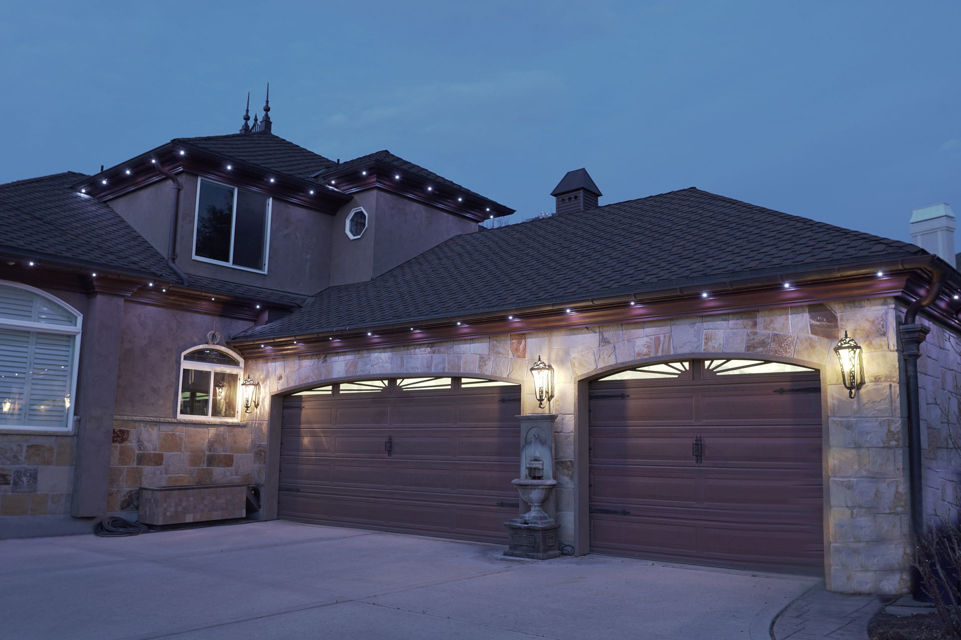 A large house with three garage doors is lit up at night with christmas lights.