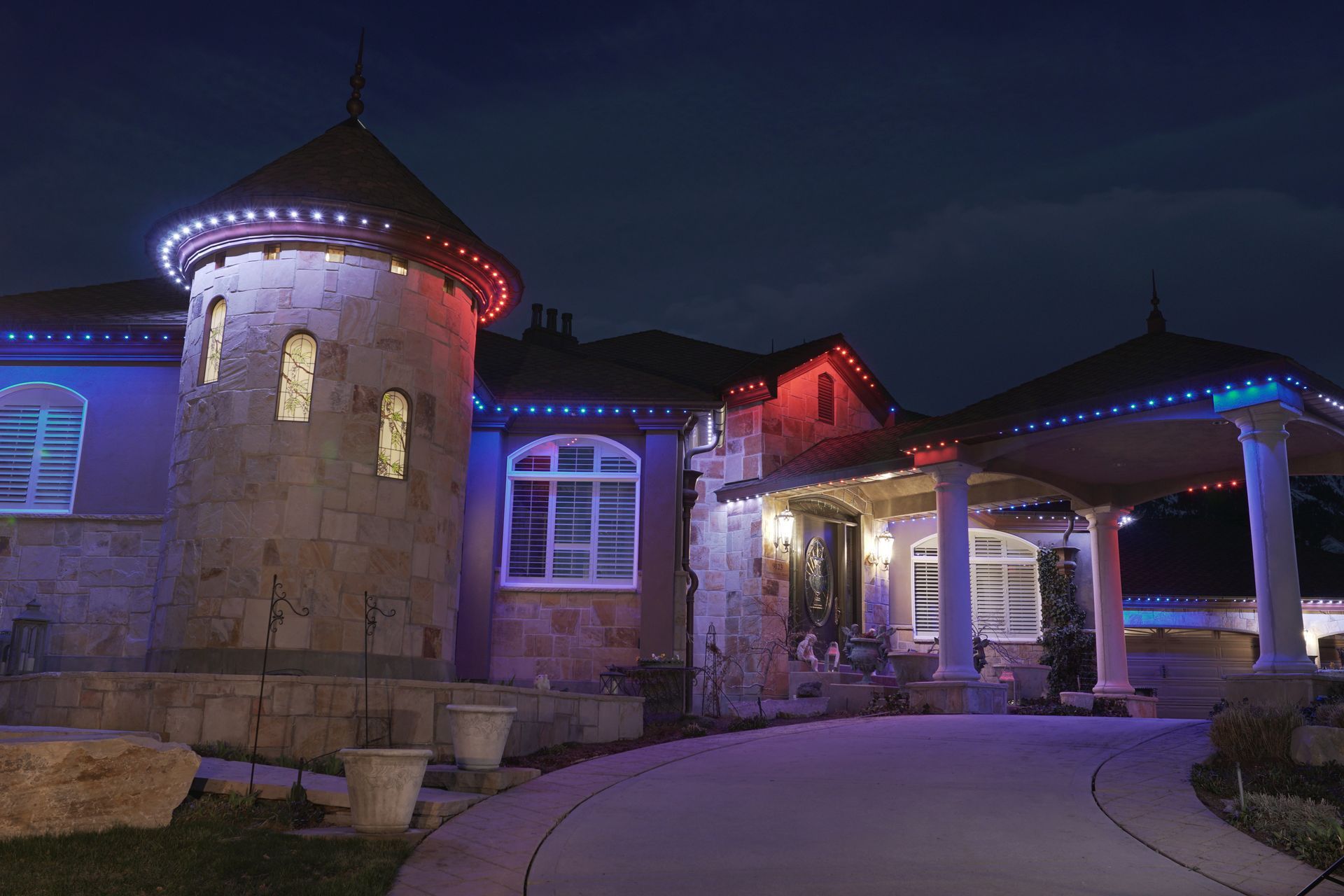 A large house is lit up with red , white and blue lights at night.