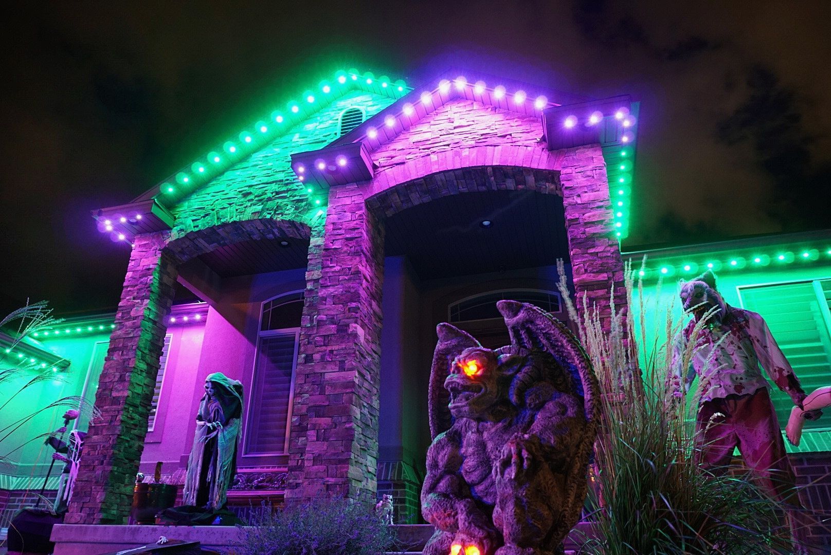 A house decorated for halloween with purple and green lights and a gargoyle statue.