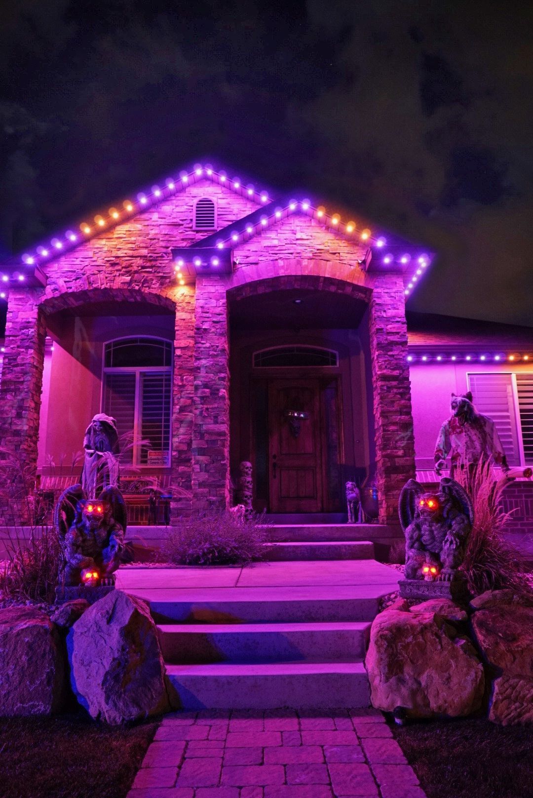 A house is decorated for halloween with purple lights and skeletons.