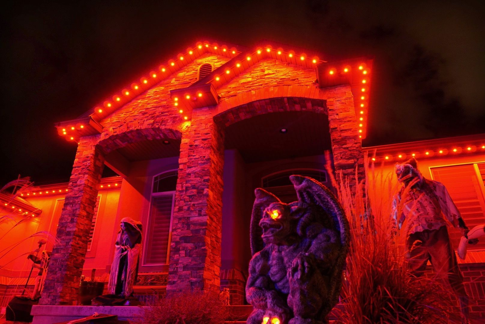 A house is decorated for halloween with red lights and a gargoyle statue.